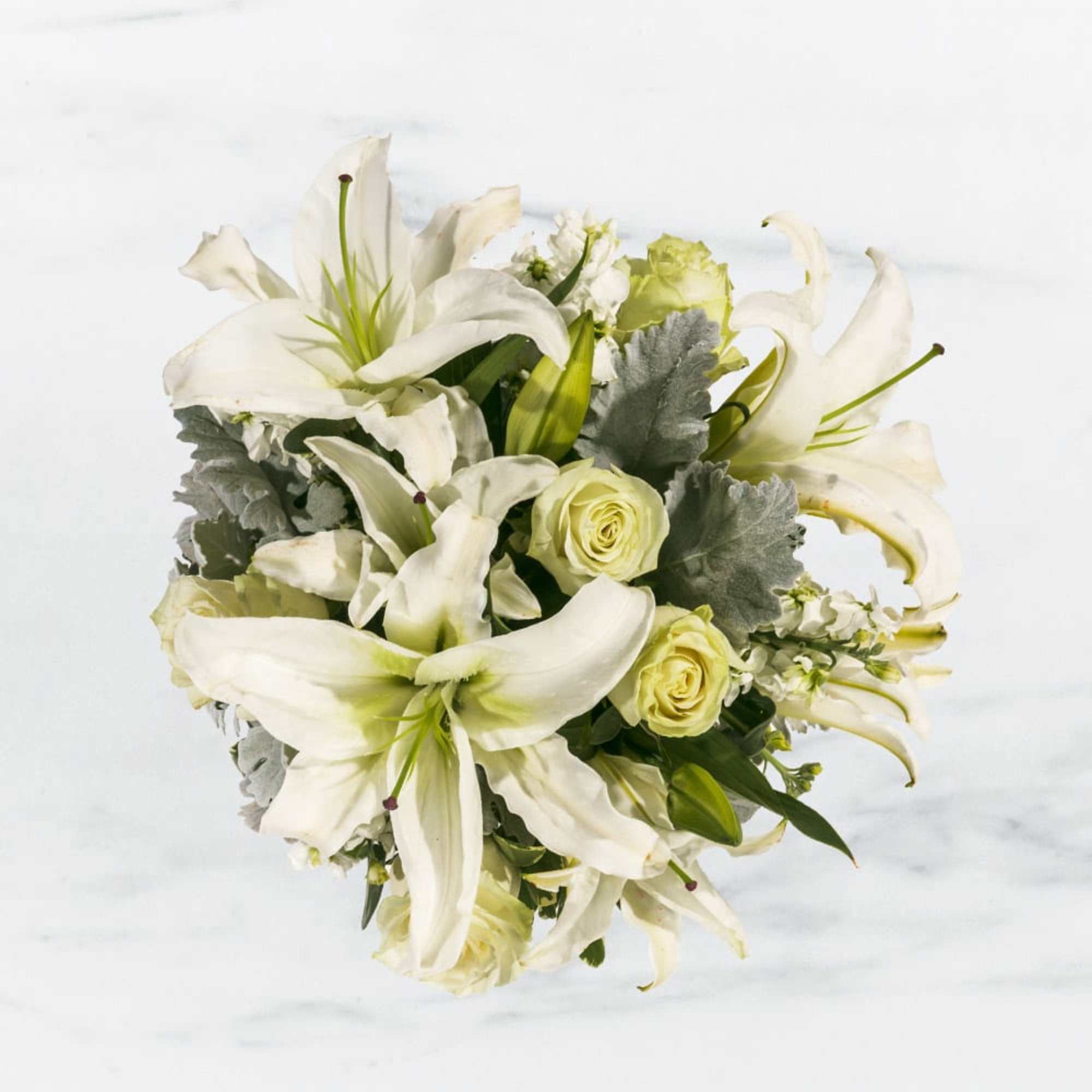 This arrangement includes white roses, white asiatic lilies, white stock, and dusty