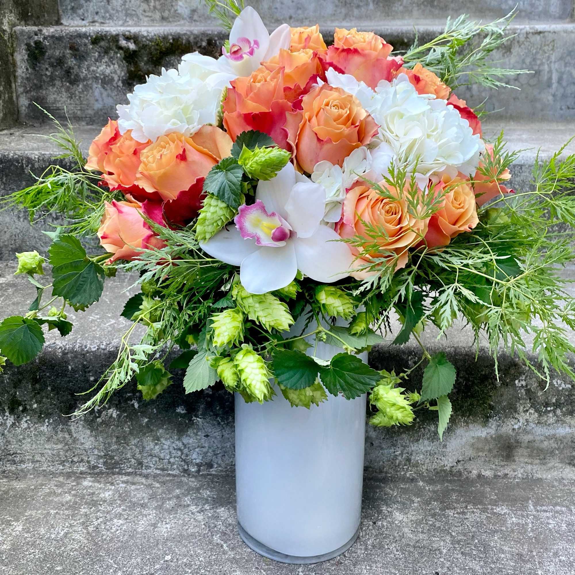 Bouquet of peach and white roses with orchids in a tall white vase