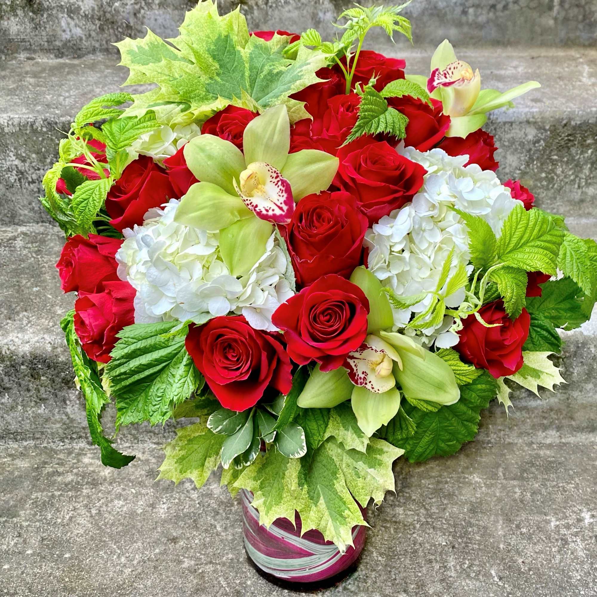 Red roses and white hydrangeas in a wrapped vase with green orchids