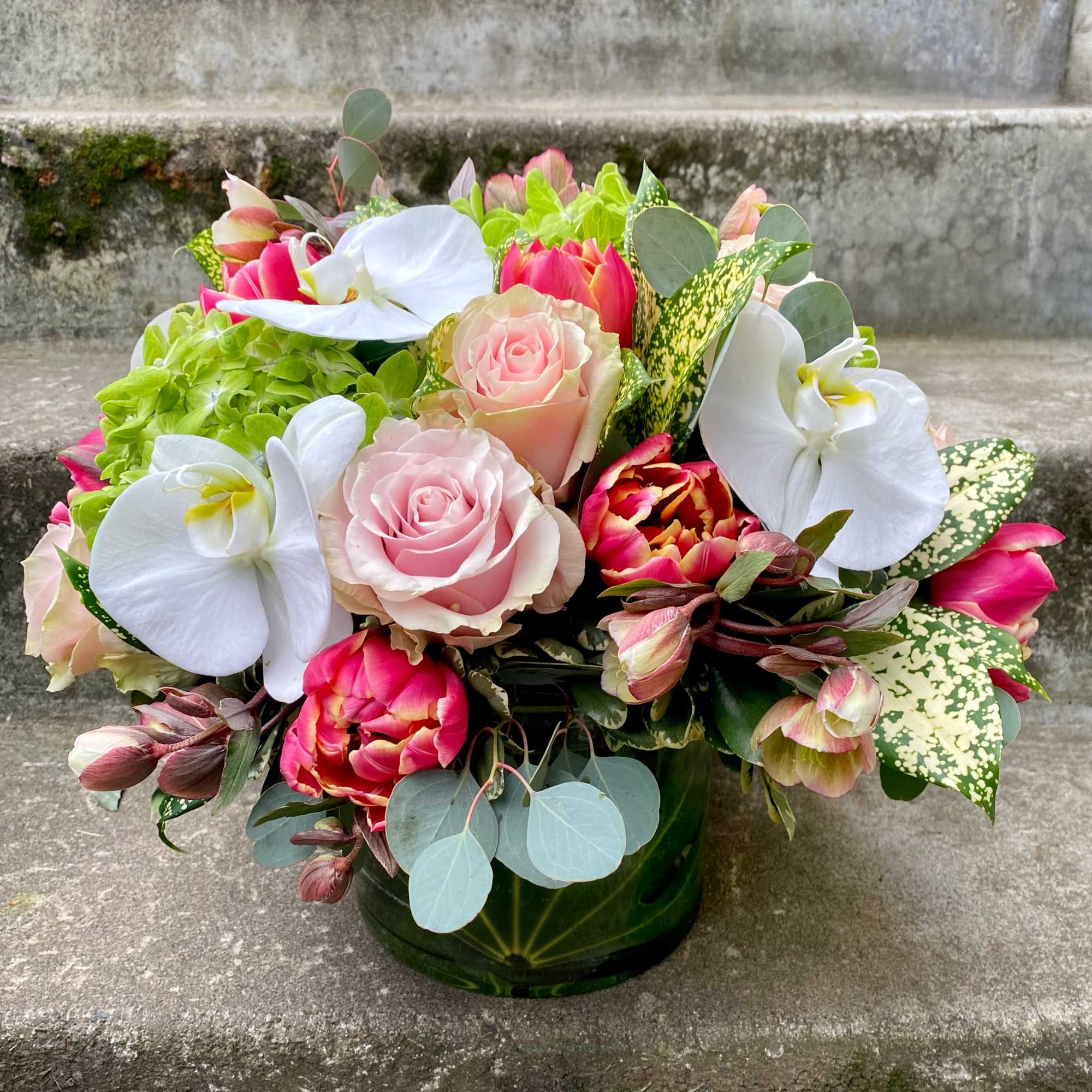 Bouquet of pink roses, white orchids, and tulips in a green vase