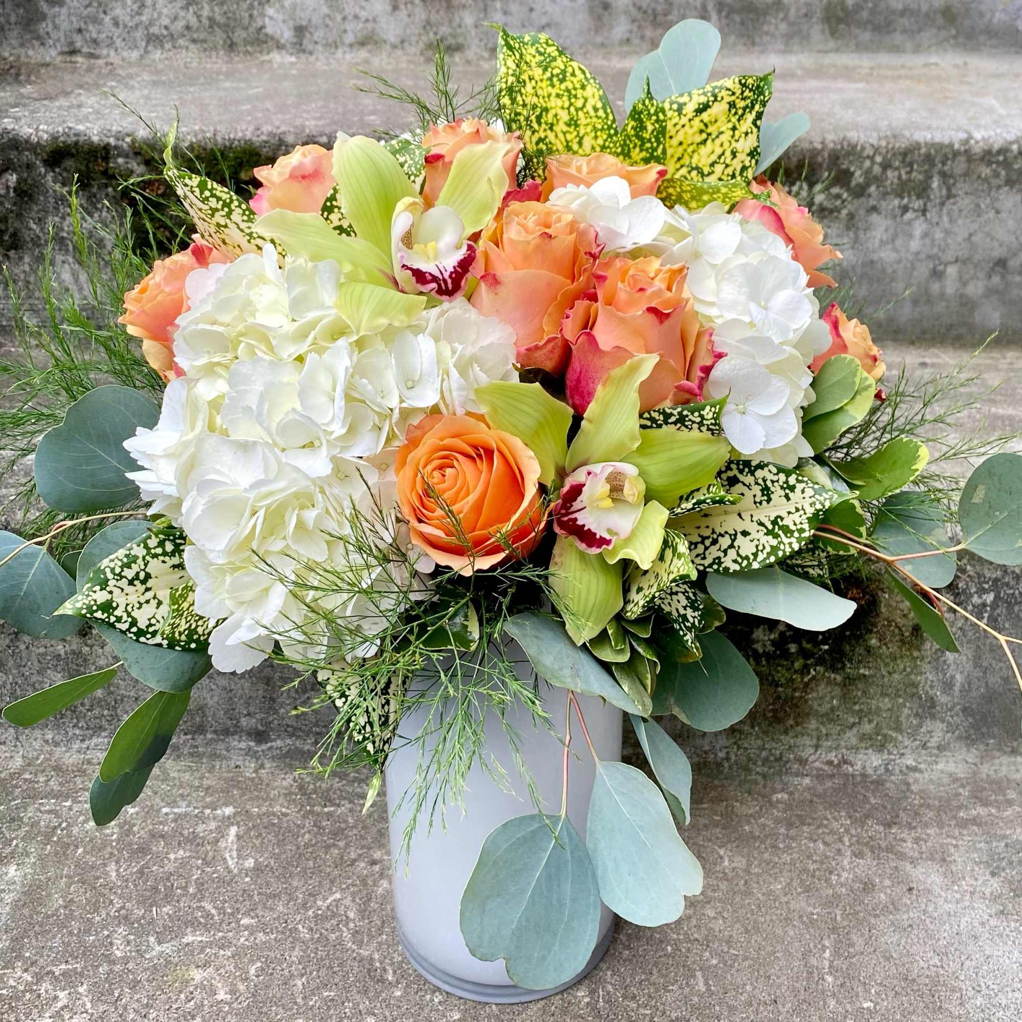 Orange roses and white hydrangeas in a gray vase with mixed greenery