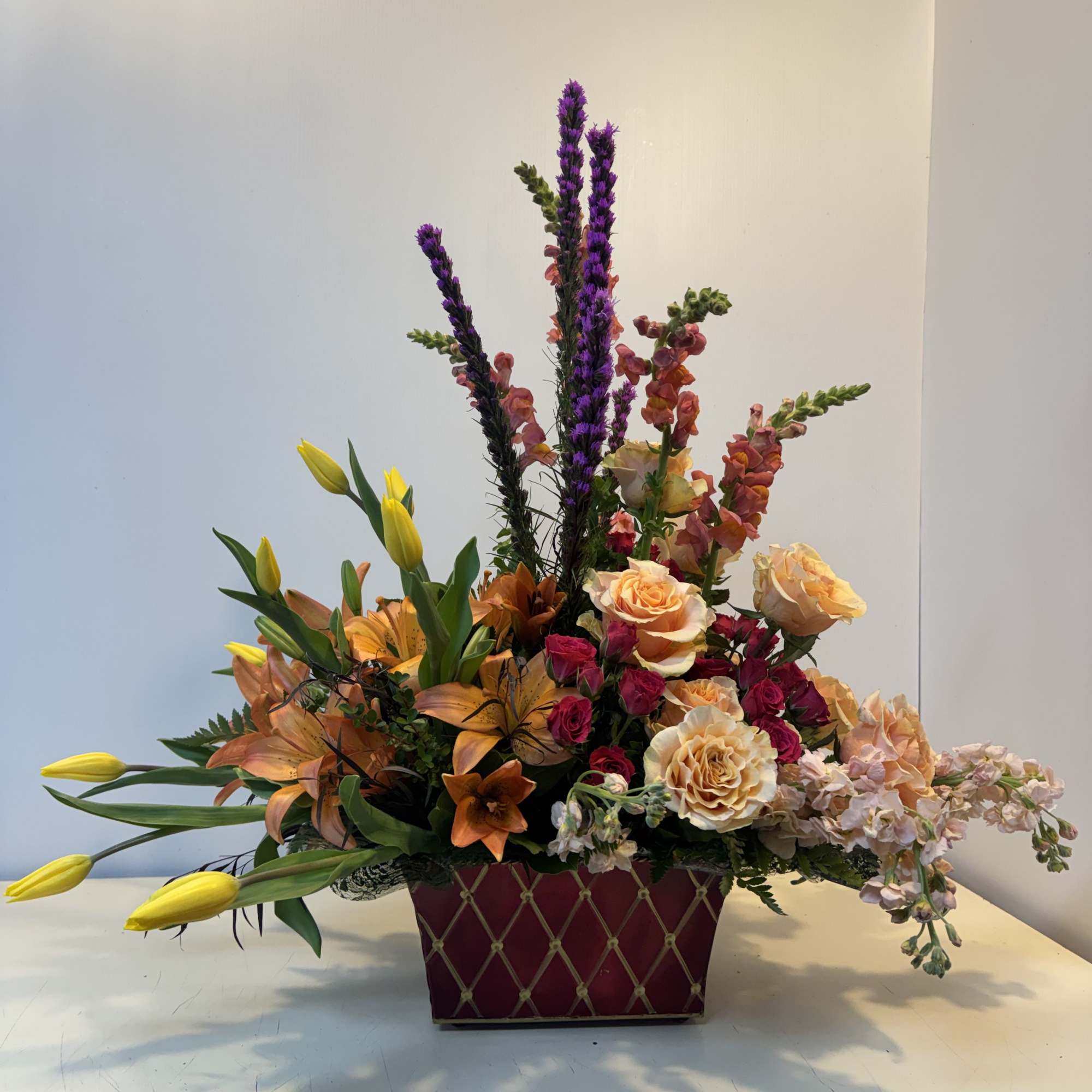 Mixed bouquet in a burgundy rectangular container with roses and lilies