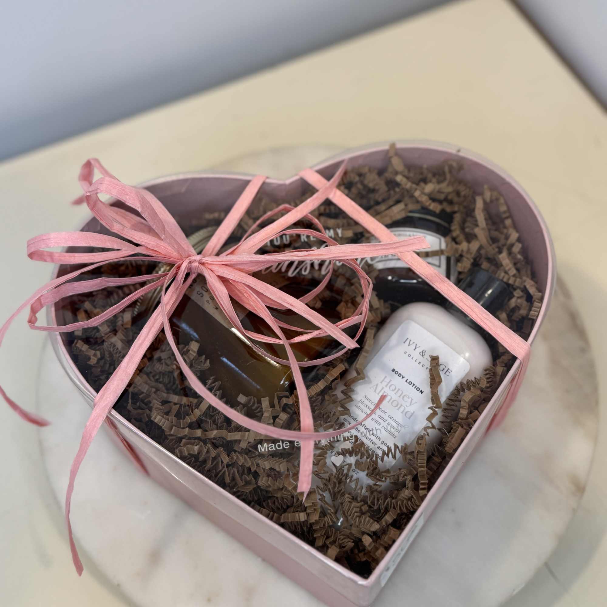 Heart-shaped gift box with bath and body items tied with a pink ribbon