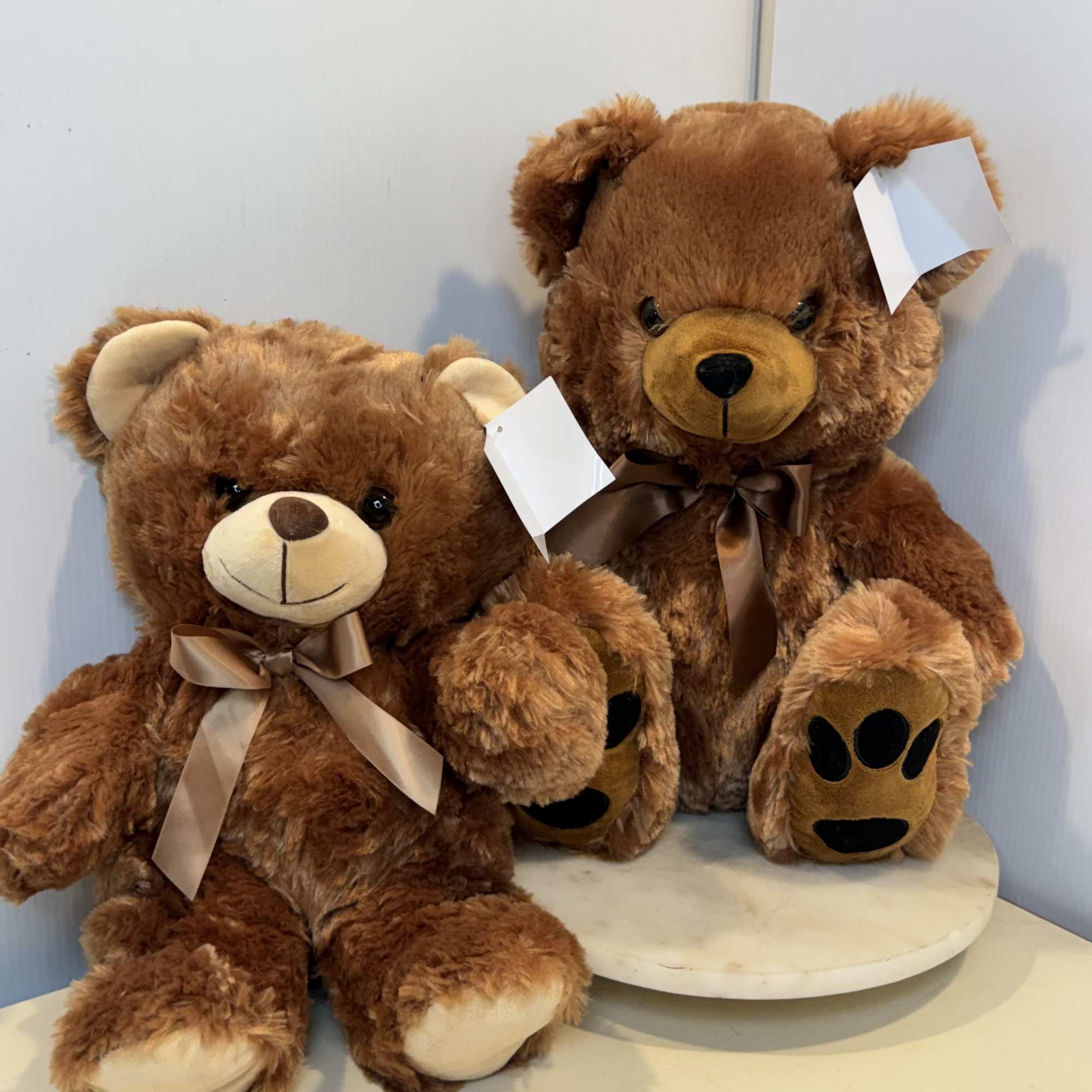 Two brown teddy bears with satin bows, one seated on a round stand