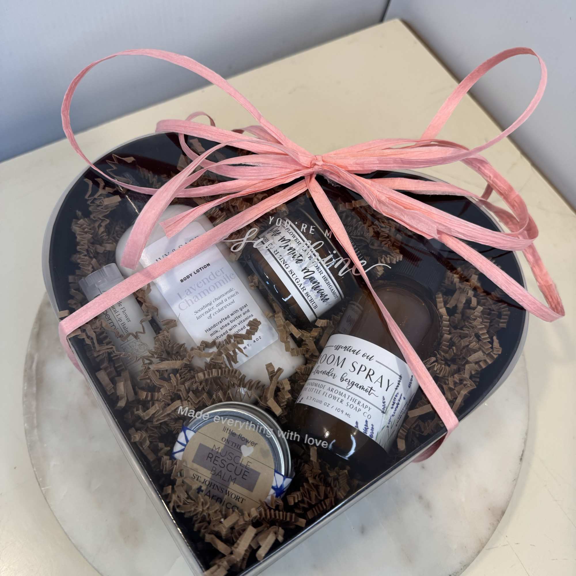 Heart-shaped gift box with bath and body products tied with a pink ribbon