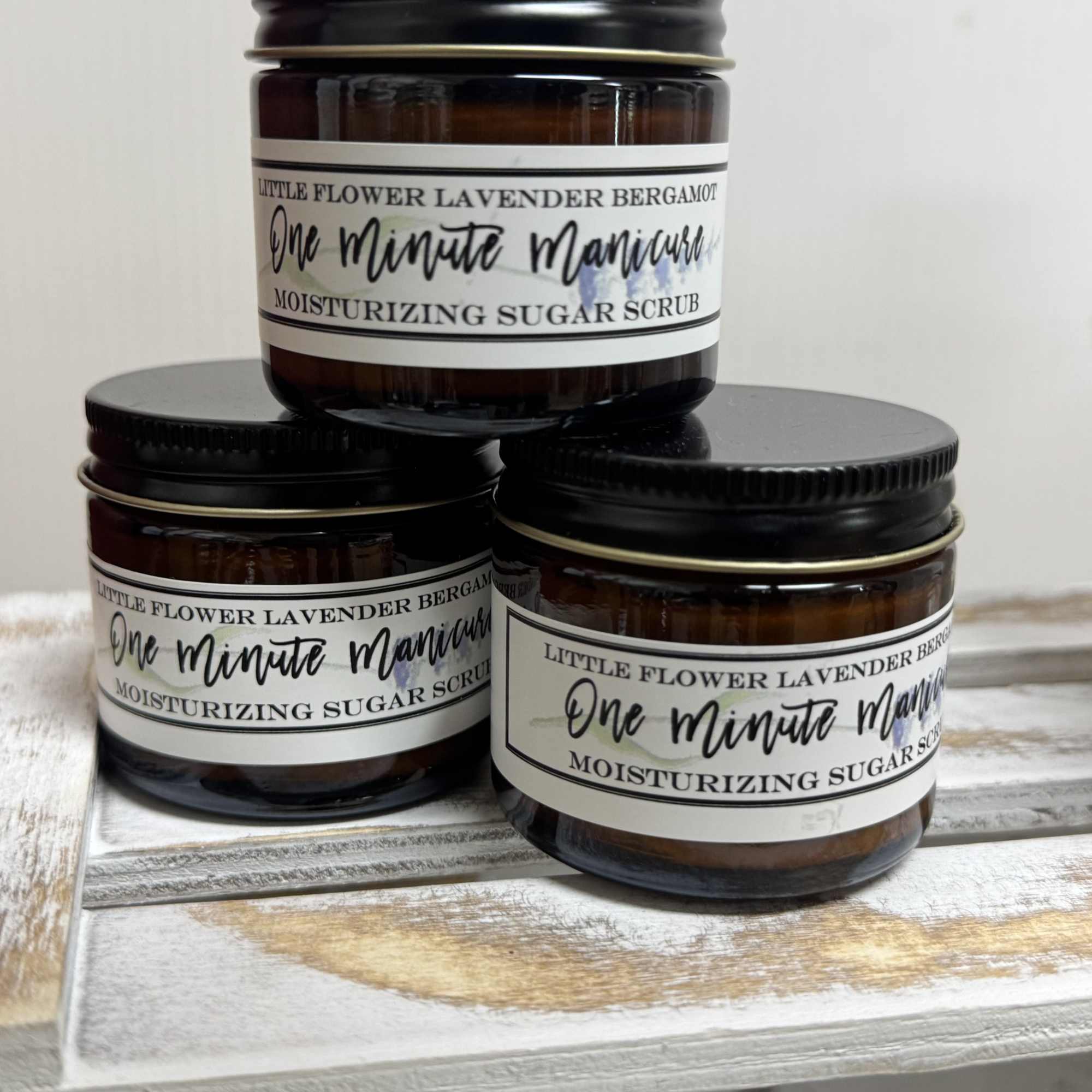 Three amber jars of lavender bergamot sugar scrub stacked on a wooden surface.