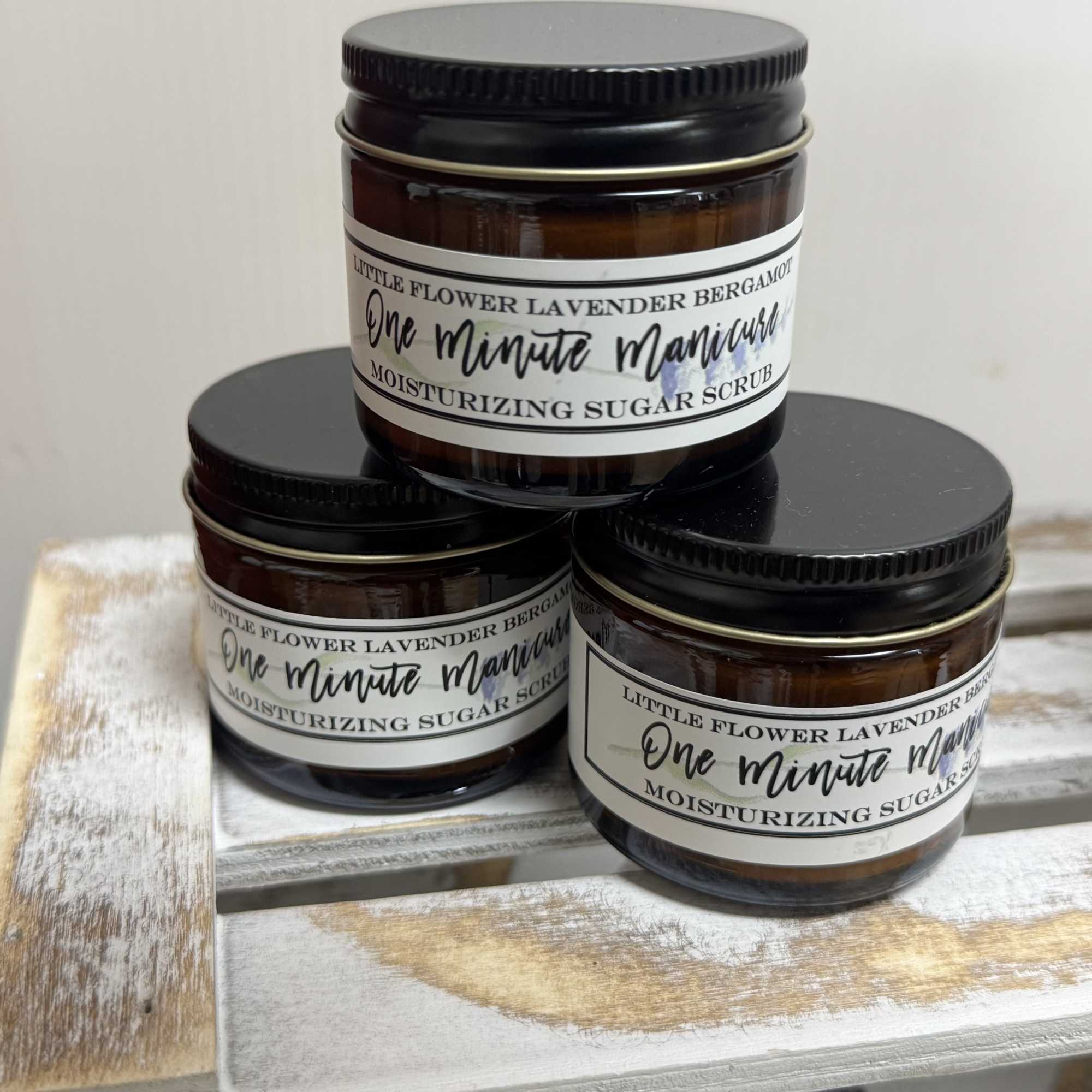 Three amber jars of moisturizing sugar scrub stacked on a wooden tray