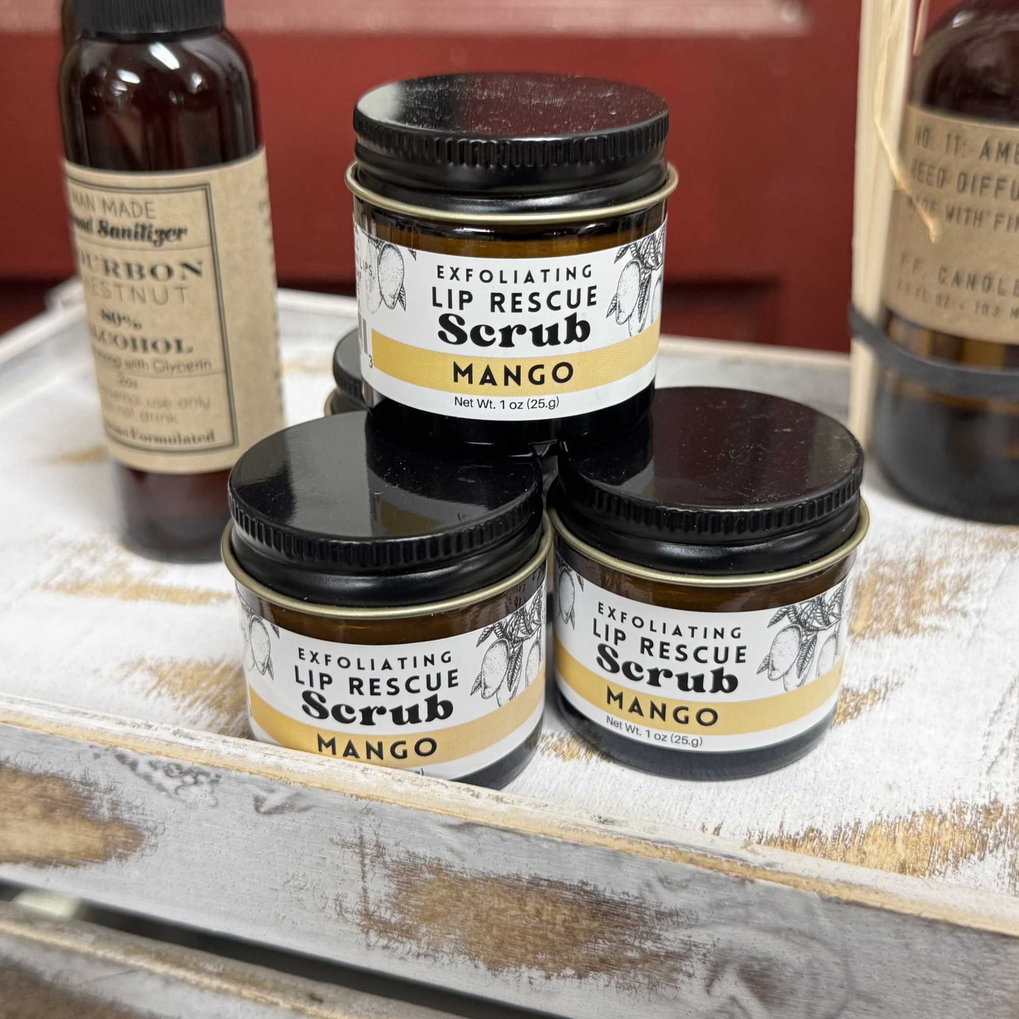 Three mango lip scrub jars and two spray bottles on a tray