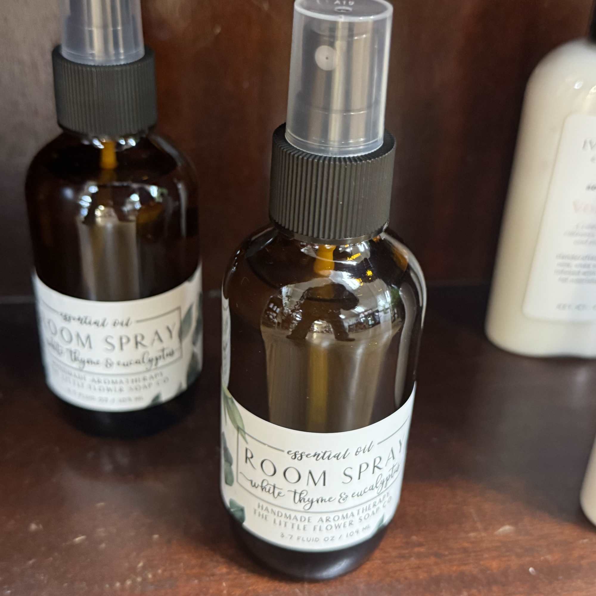 Two amber room spray bottles with clear caps sit on a wooden shelf.