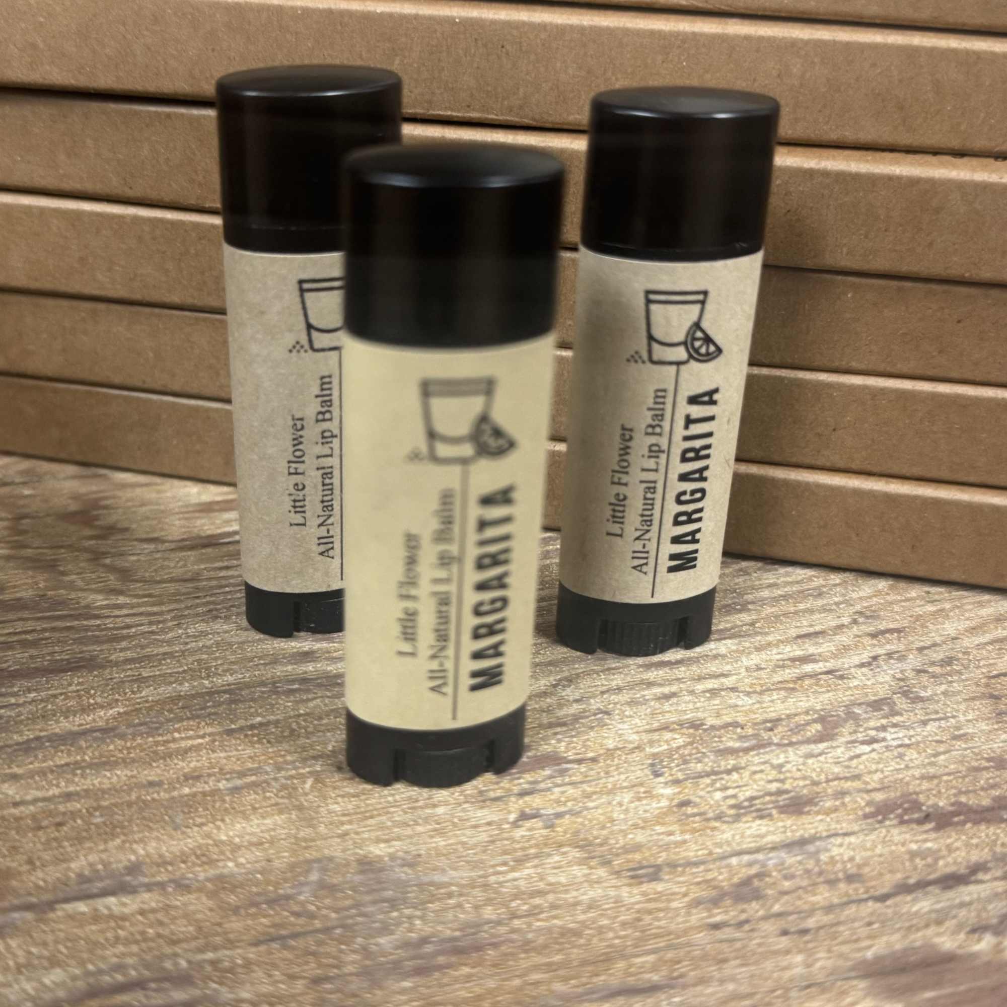 Three lip balm tubes labeled Margarita on a wooden surface