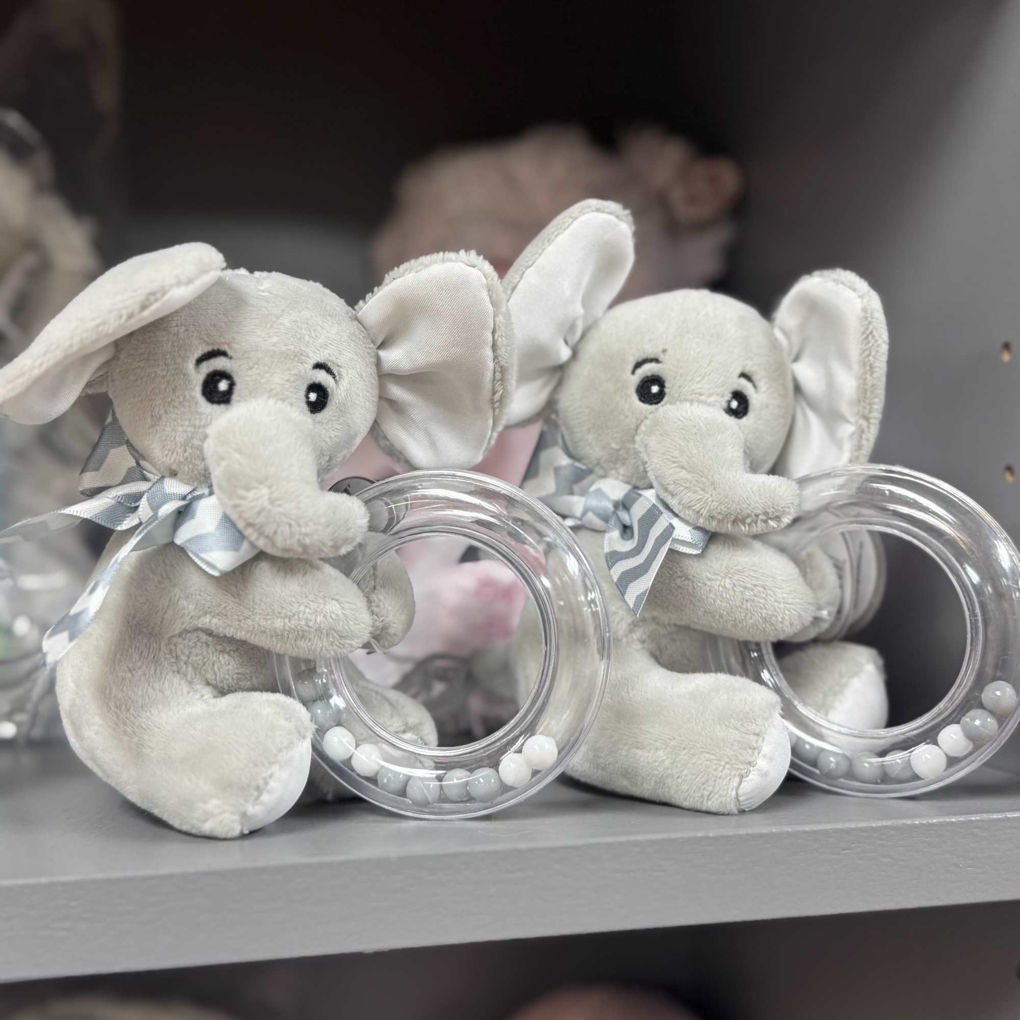Two plush elephant toys sit beside clear bead rings on a shelf.