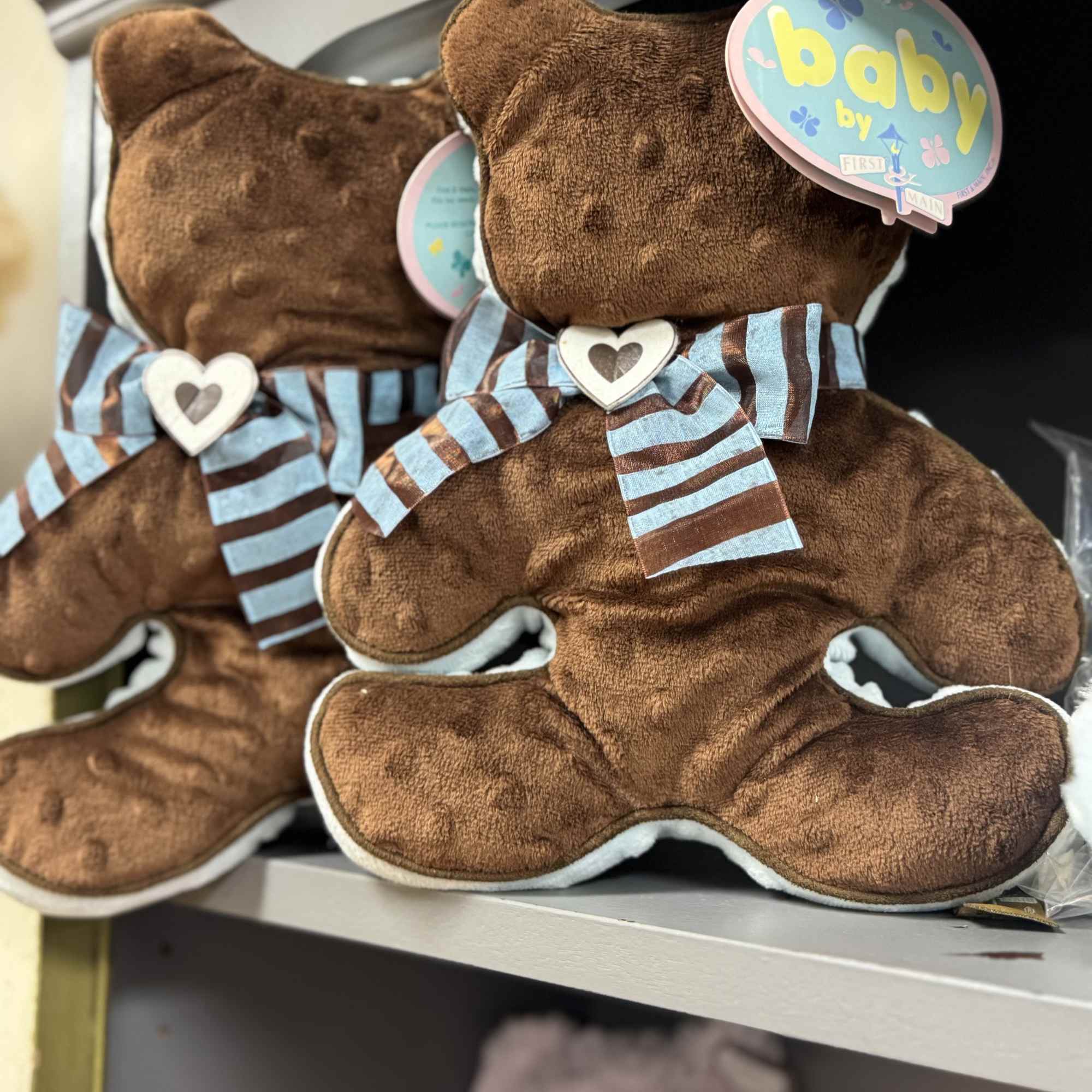 Two teddy bears with baby tags and striped bows on a shelf