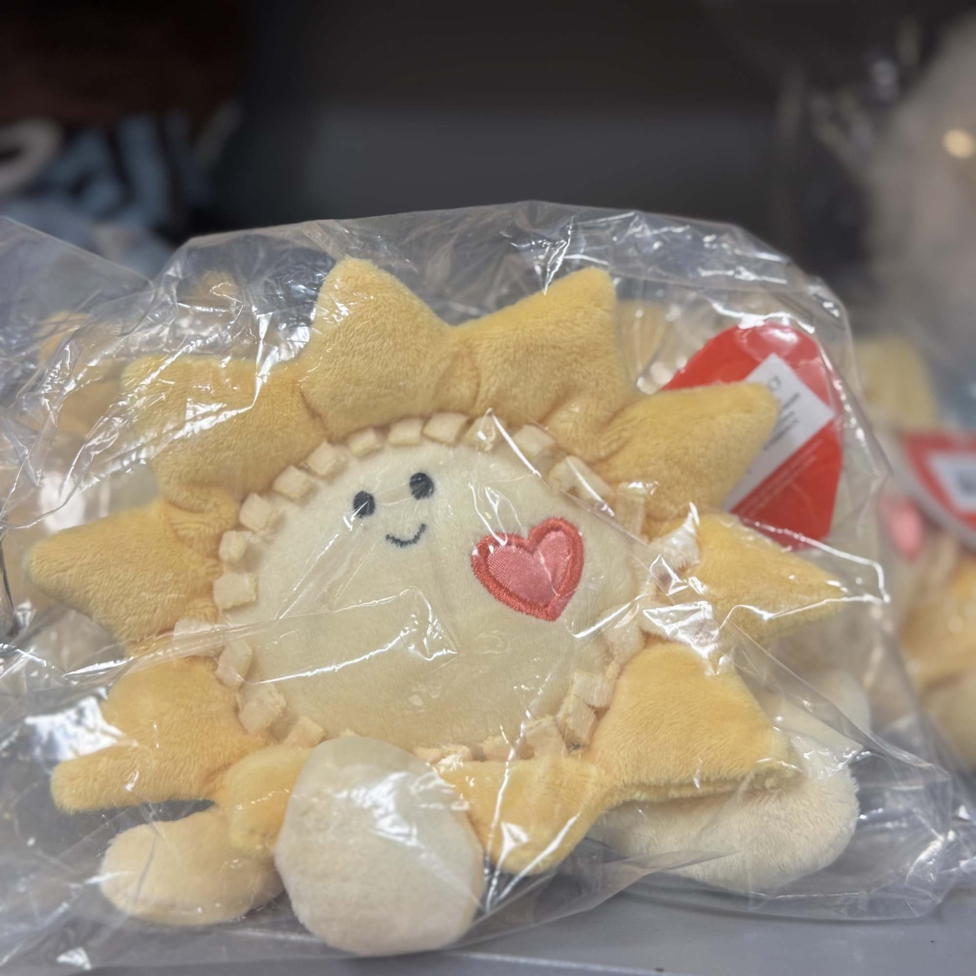 Plush sun-shaped toy in a clear plastic bag with a heart patch