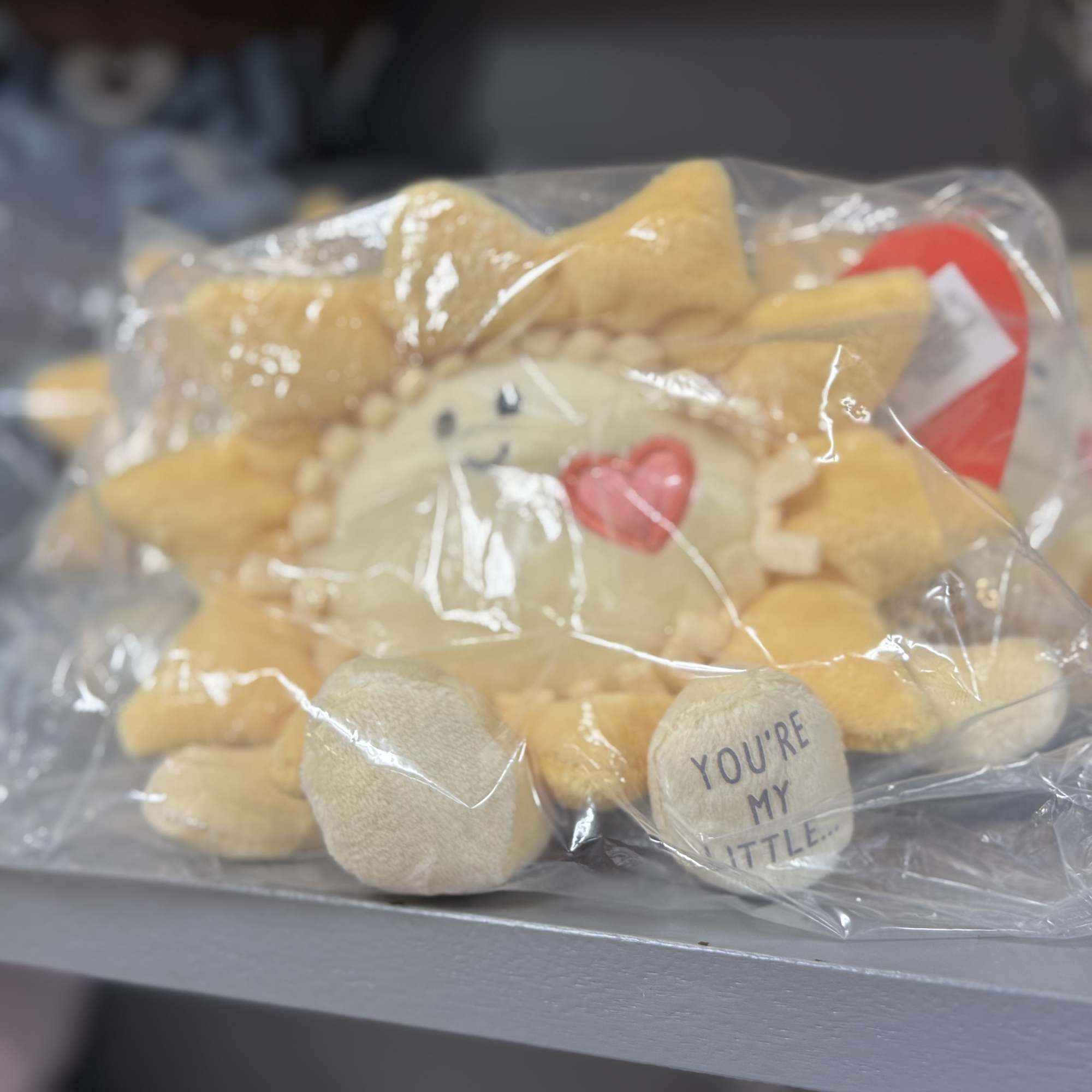 Plush sun-shaped toy in clear plastic wrapping with a small heart