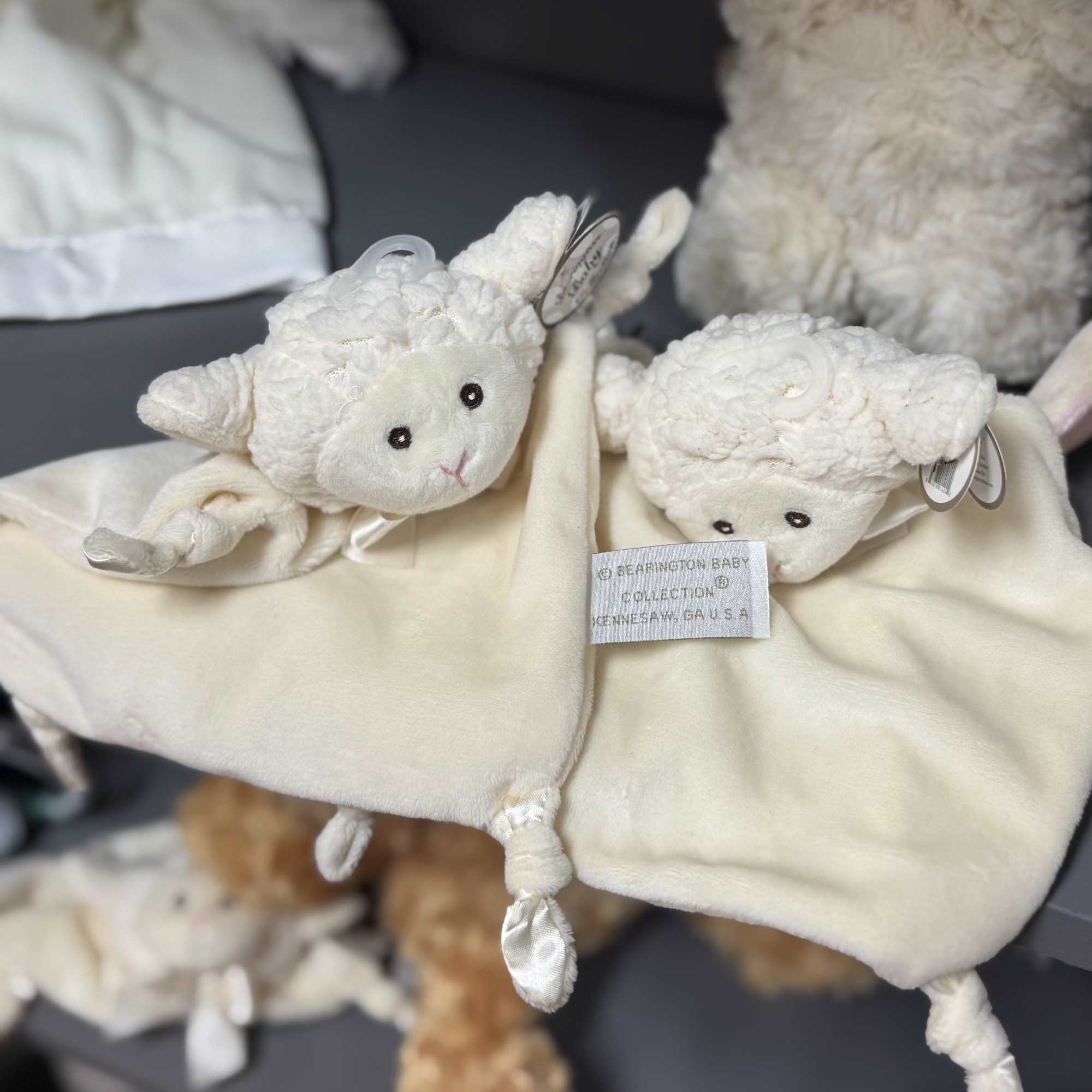 Two cream-colored plush lamb toys with a blanket