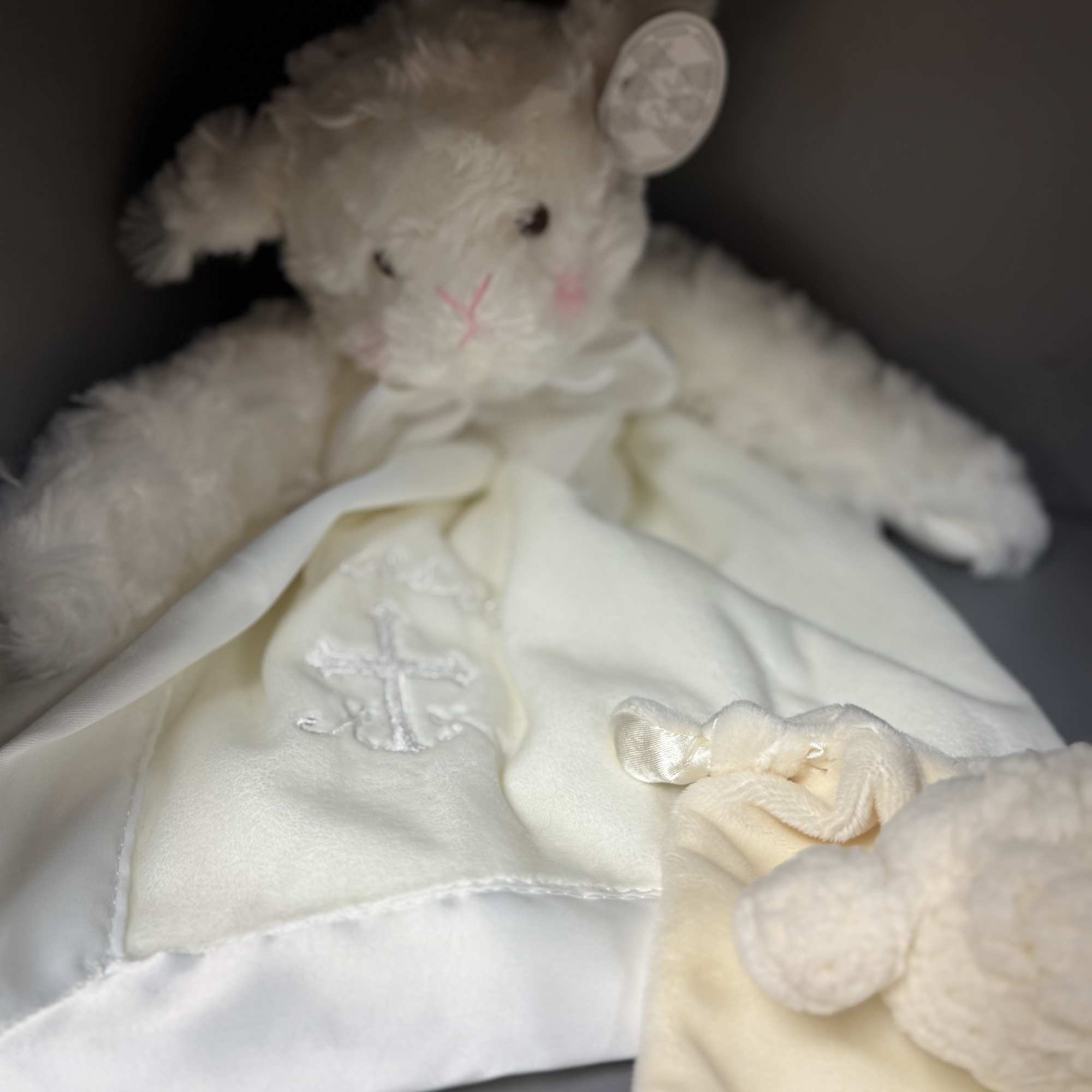 White plush teddy bear holding a satin blanket with a cross embroidery