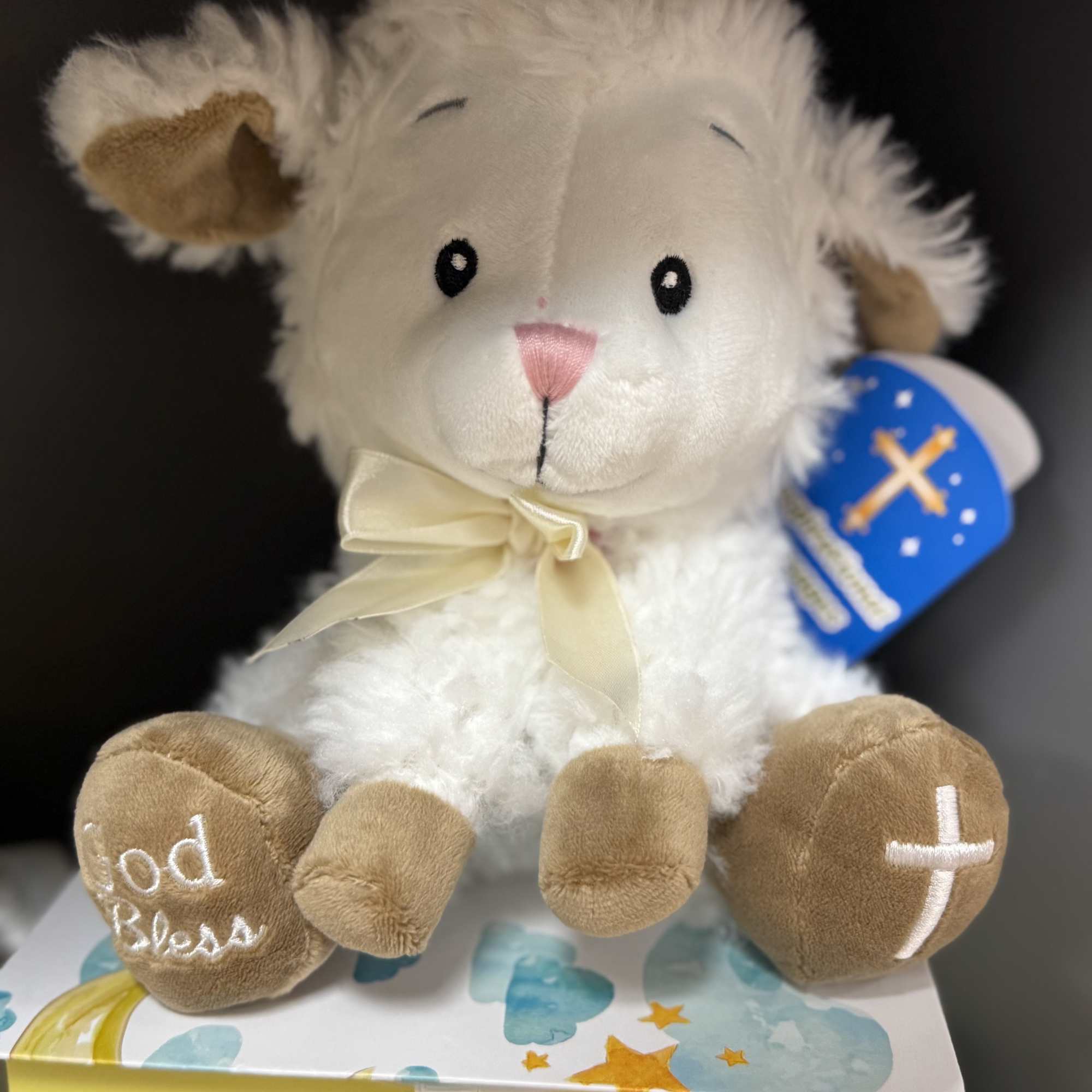 Plush lamb toy with a ribbon bow sitting on a decorated gift box