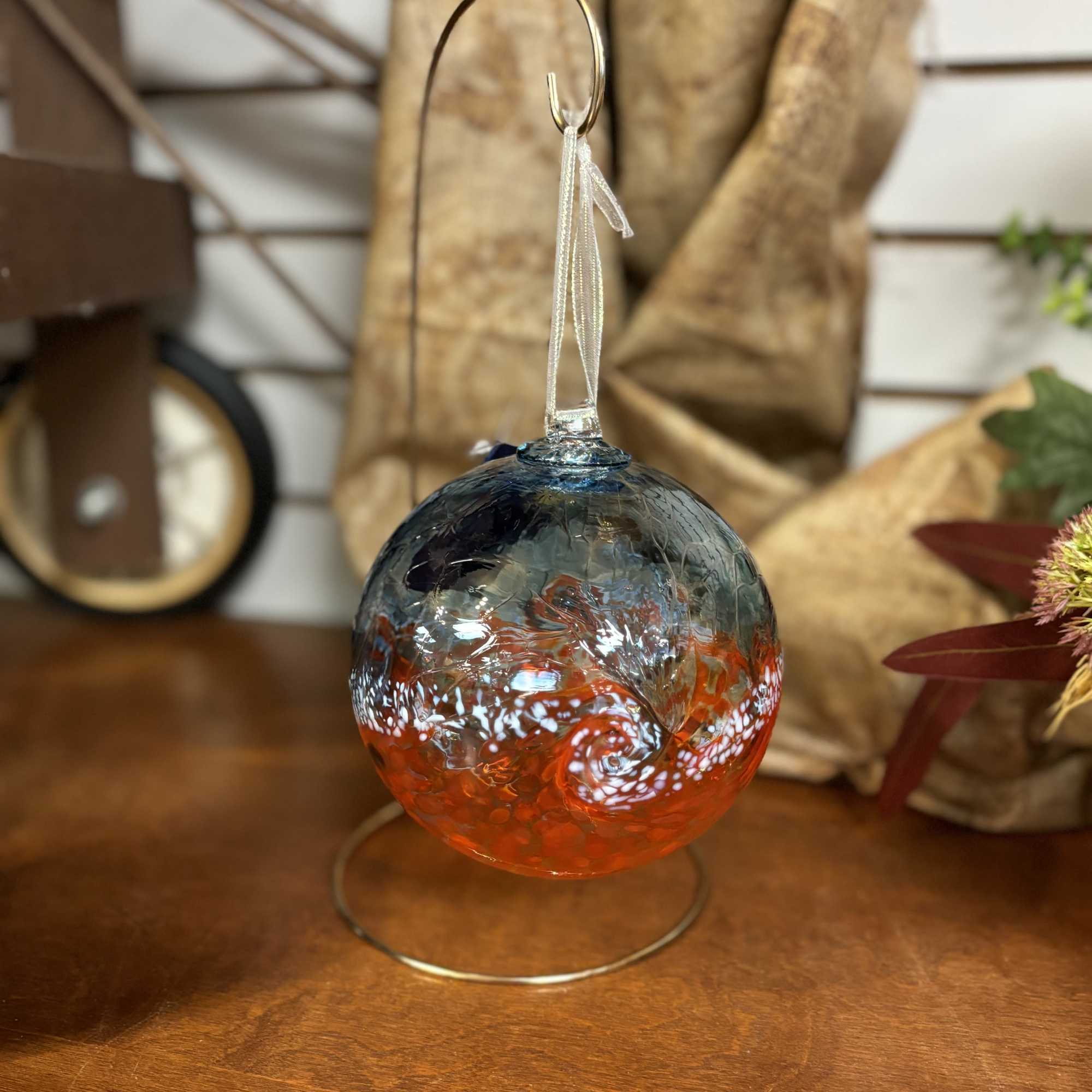 Glass ornament with blue and orange swirls hanging on a metal stand