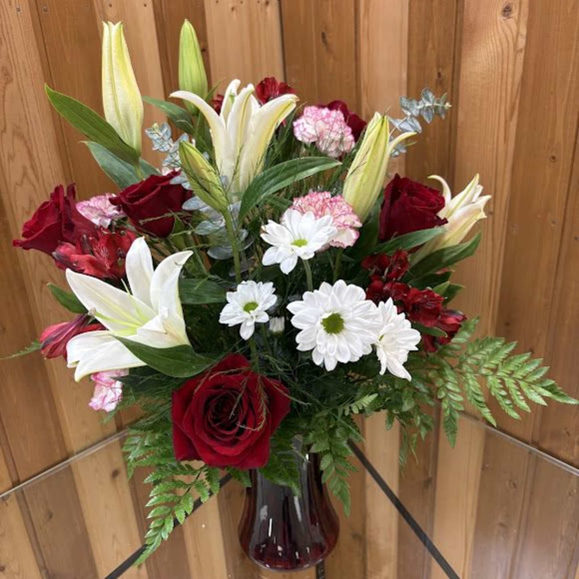 Mixed bouquet of red roses, white lilies, and daisies in a glass vase