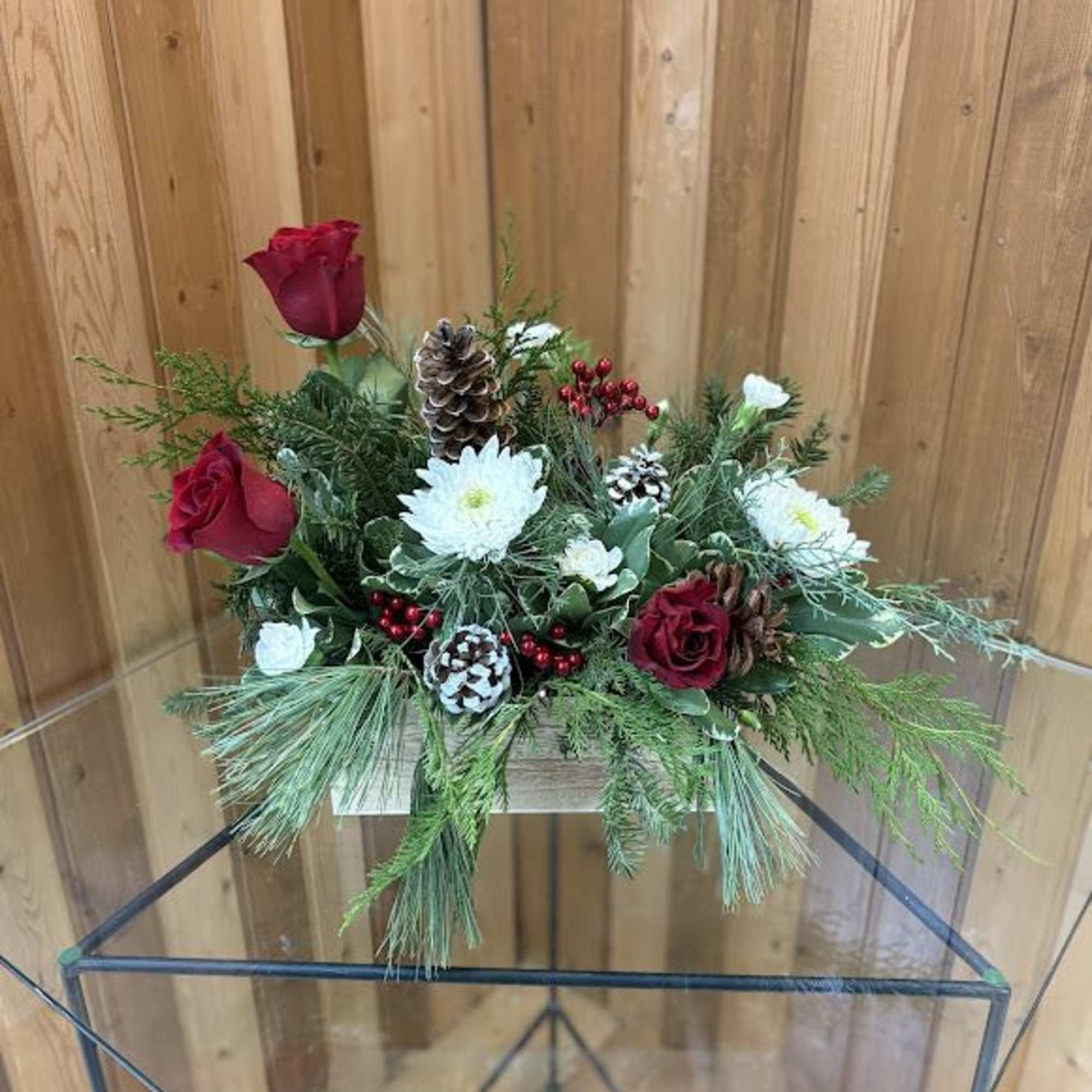 Holiday floral arrangement with red roses, white blooms, and pinecones