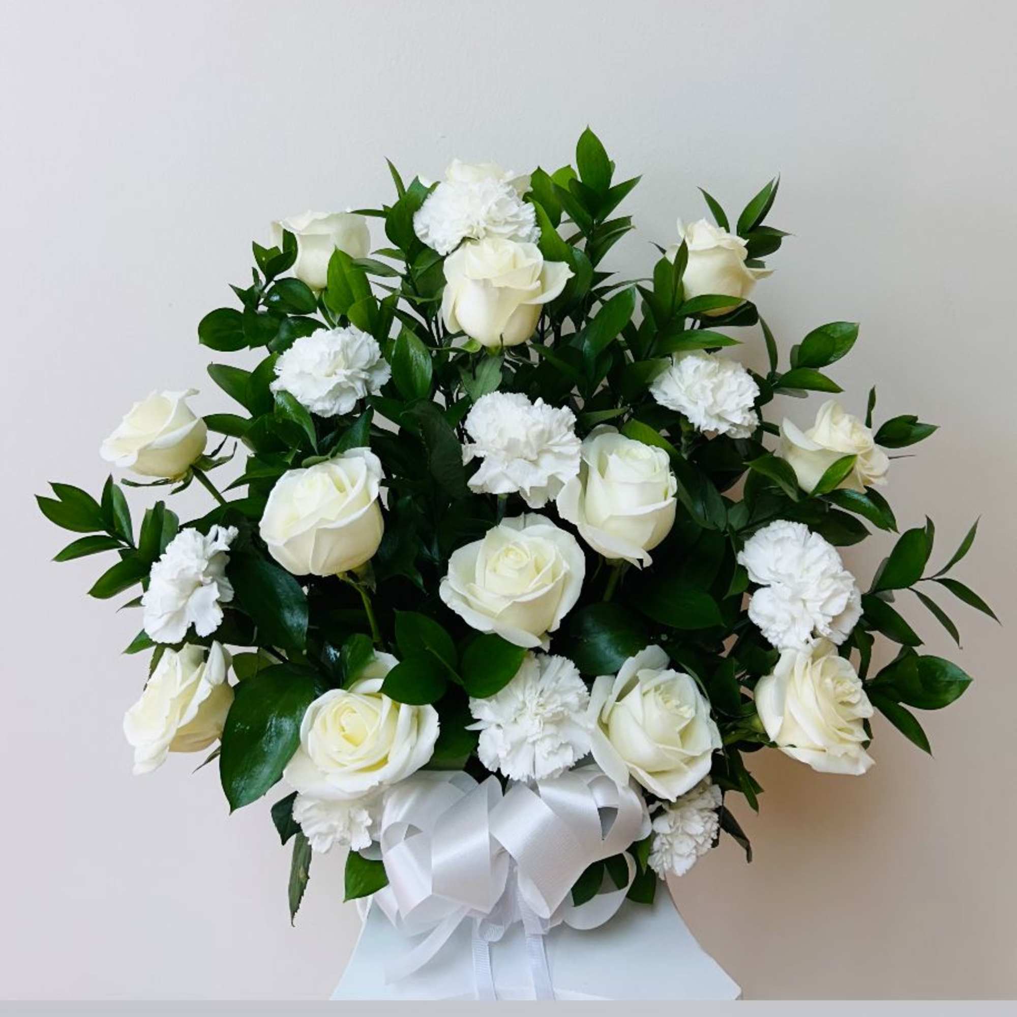 White roses and carnations arranged with a white ribbon bow