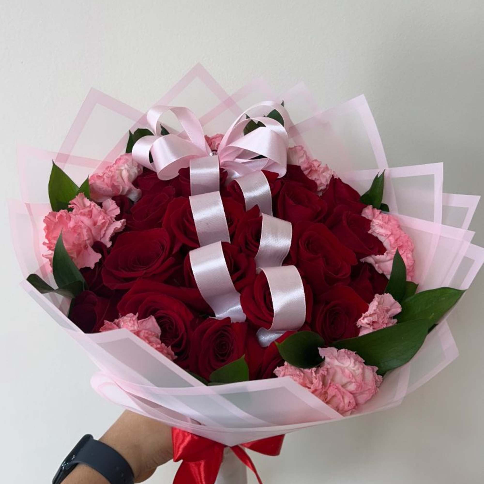 Bouquet of red roses and pink carnations wrapped in pale pink paper with a ribbon