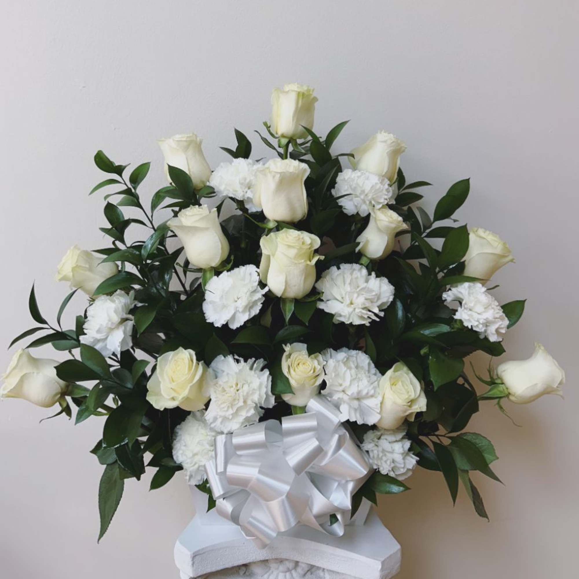 White roses and carnations arranged with greenery and a white ribbon bow