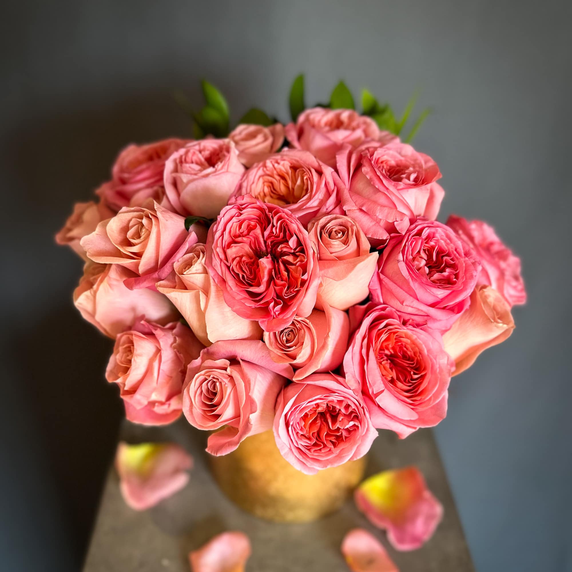 Pink roses arranged in a gold vase with scattered petals