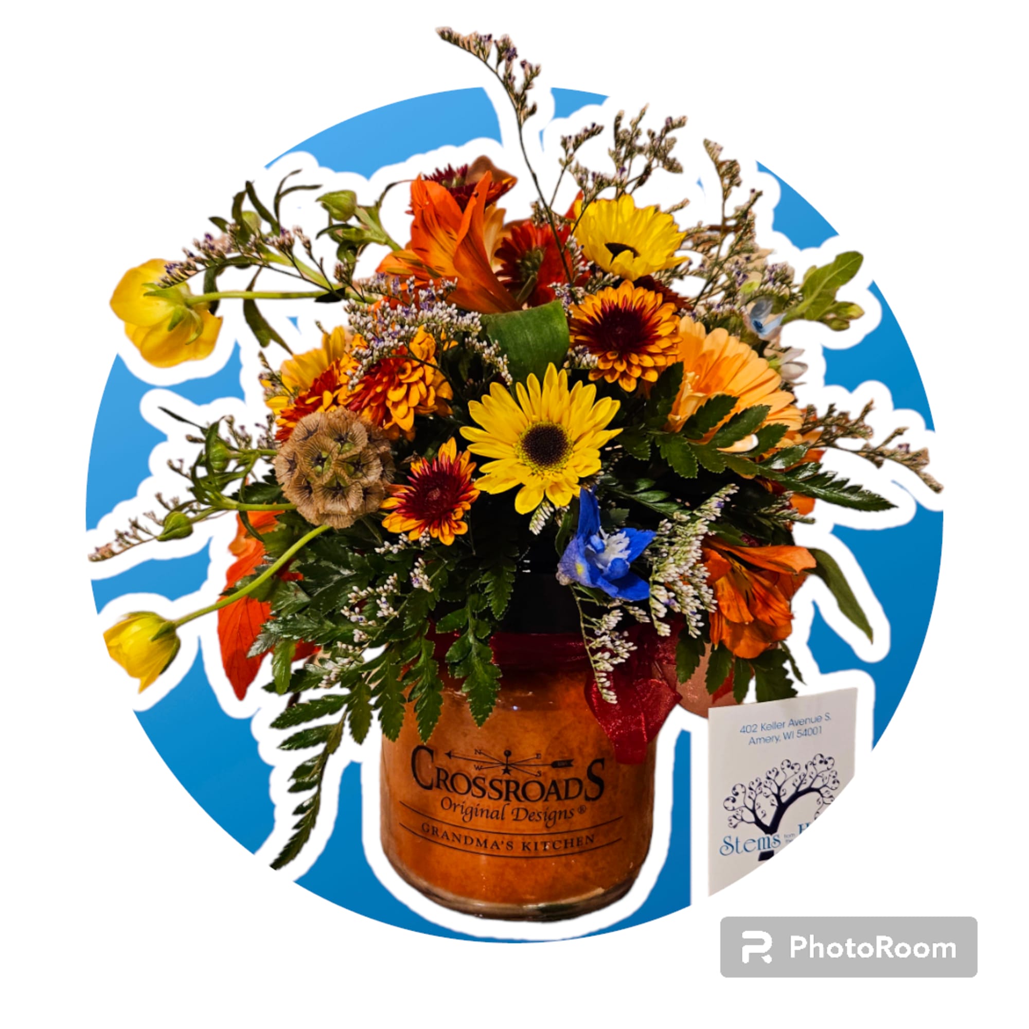 Warm-toned mixed flower arrangement in an amber Crossroads jar with a business card beside it.