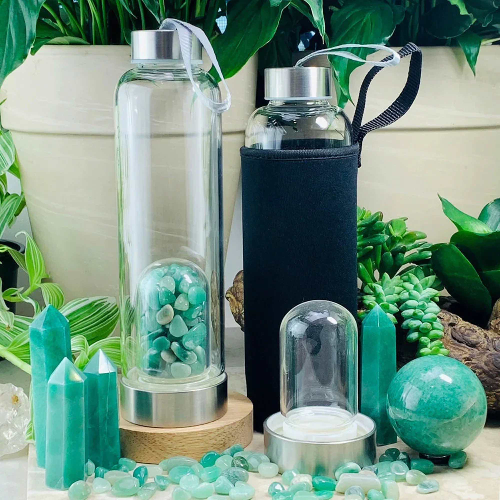 Two glass water bottles with metal caps and crystal stones beside green crystal decor.
