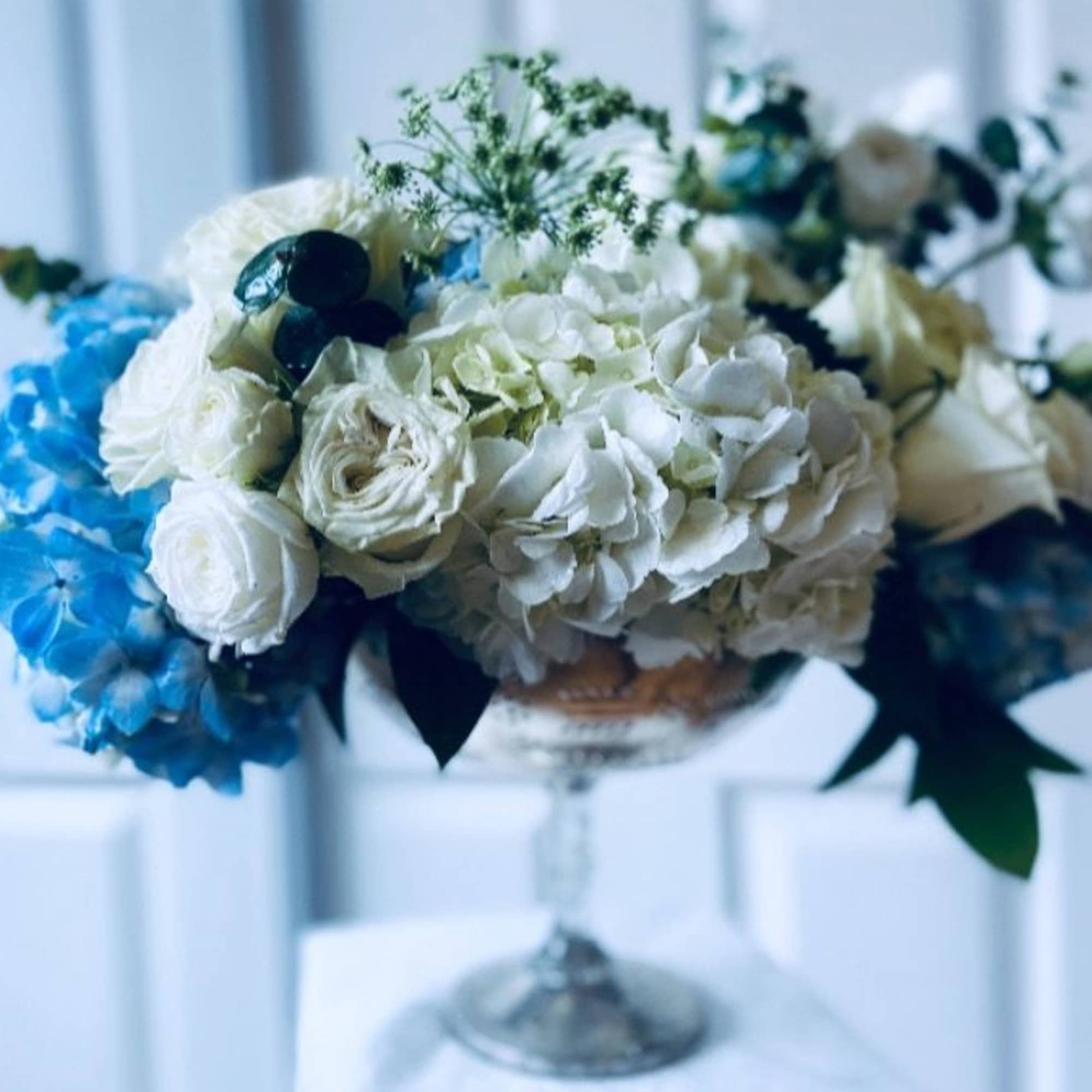 White and blue floral arrangement in a glass pedestal vase