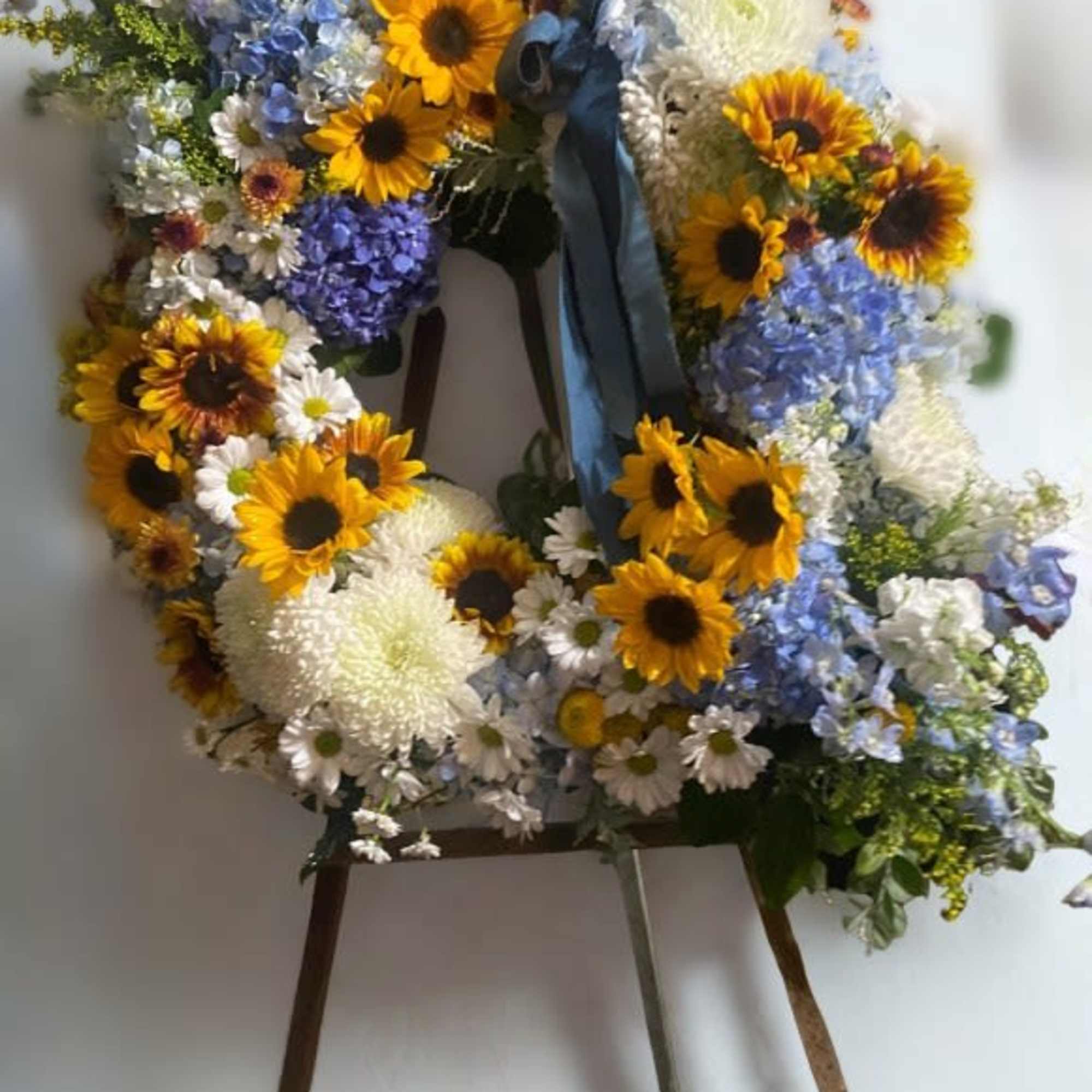Large floral wreath on an easel with sunflowers, blue hydrangeas, and white blooms