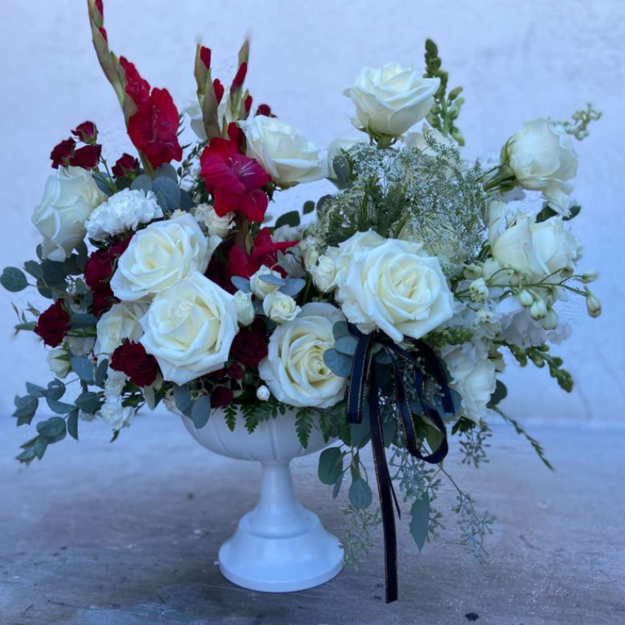White and red rose arrangement in a white pedestal vase