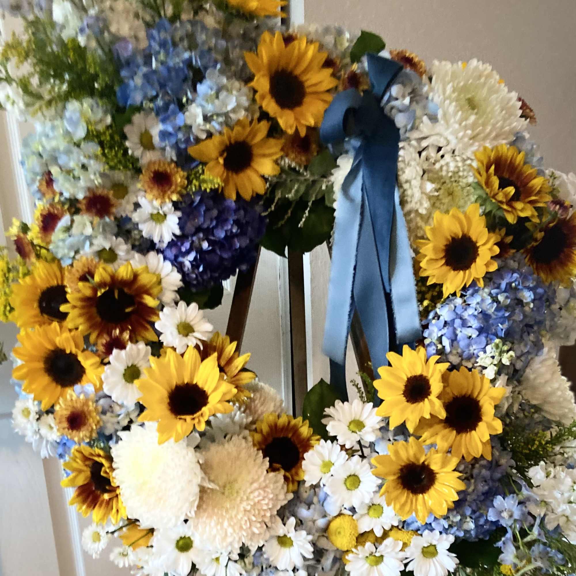 Large floral wreath with sunflowers, white daisies, and blue ribbon on an easel