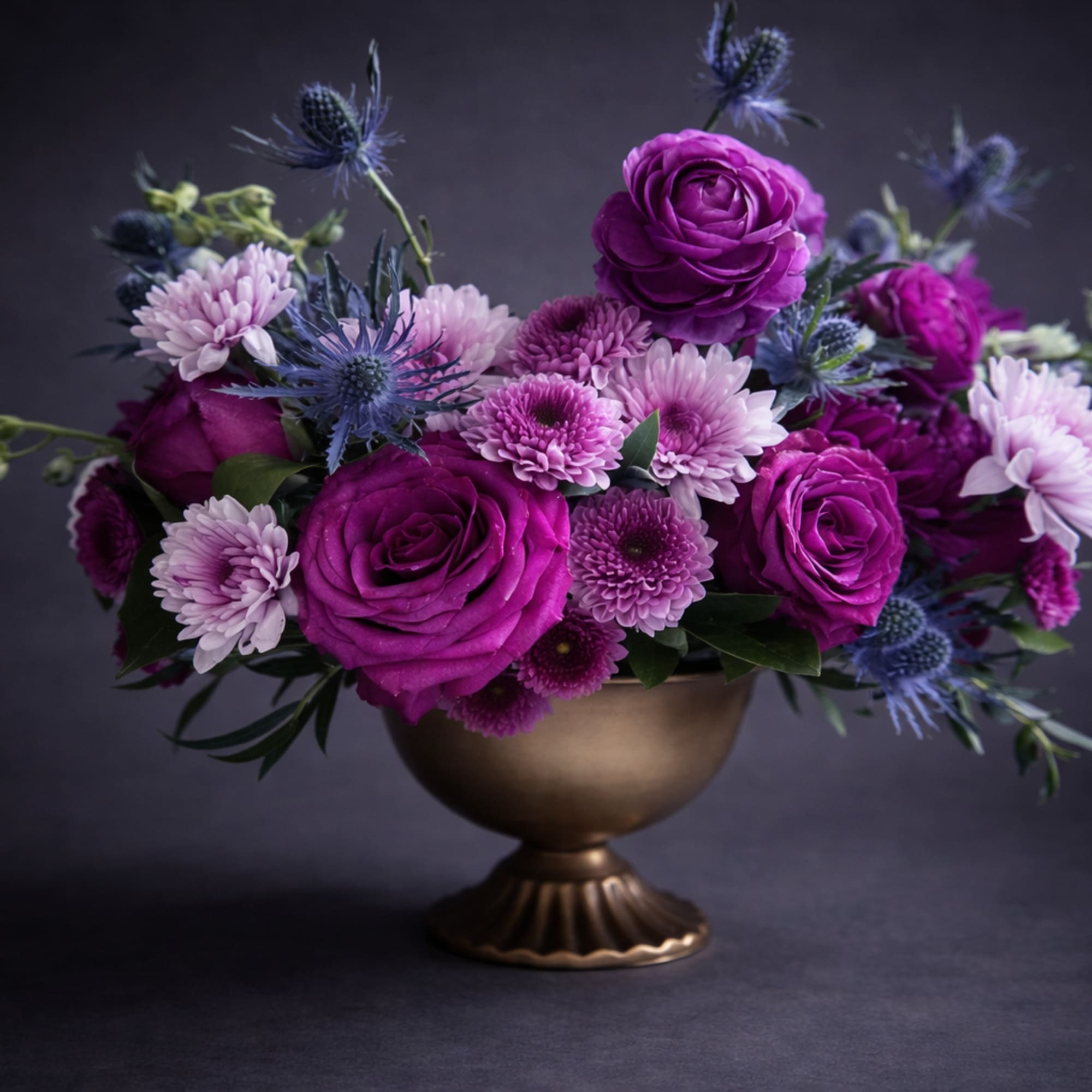 Purple and pink flowers arranged in a gold pedestal vase