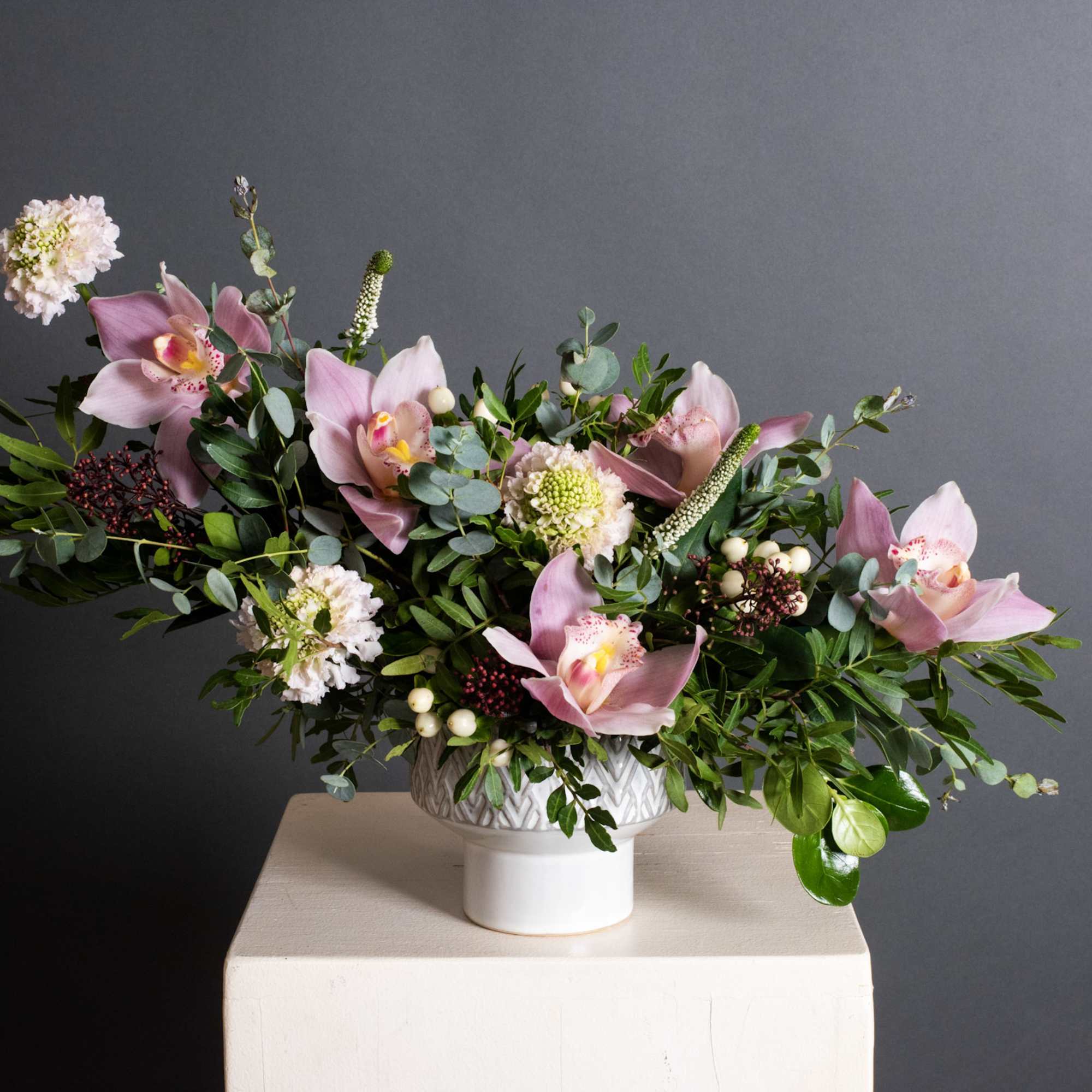Pink orchid arrangement in a white pedestal vase