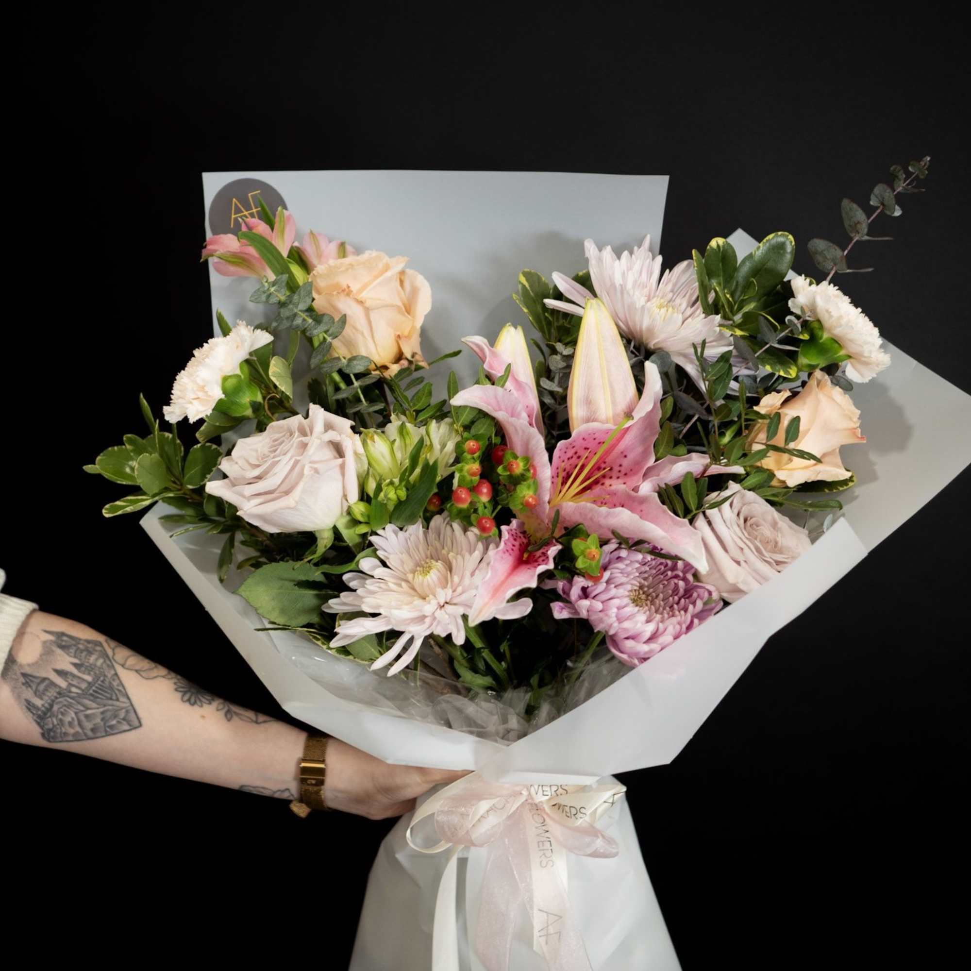 Handheld bouquet of pink and cream flowers wrapped in white paper