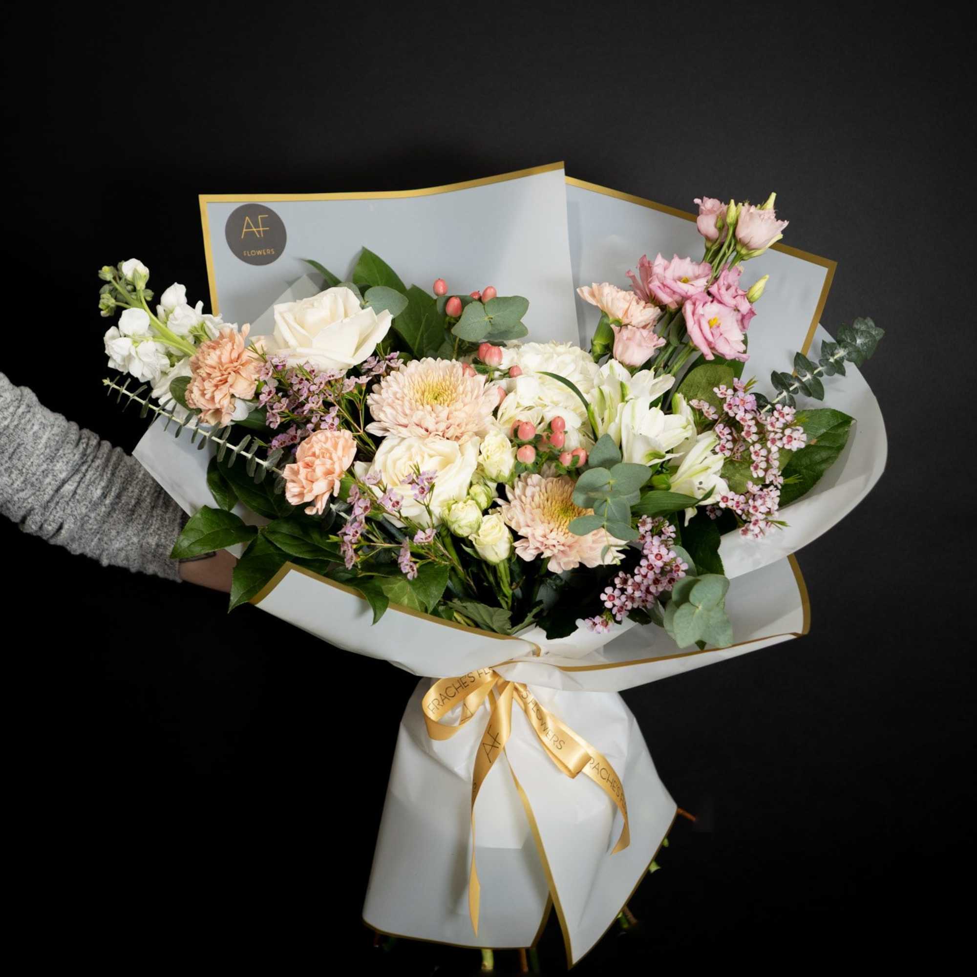 Handheld bouquet of pink and white flowers wrapped in white paper