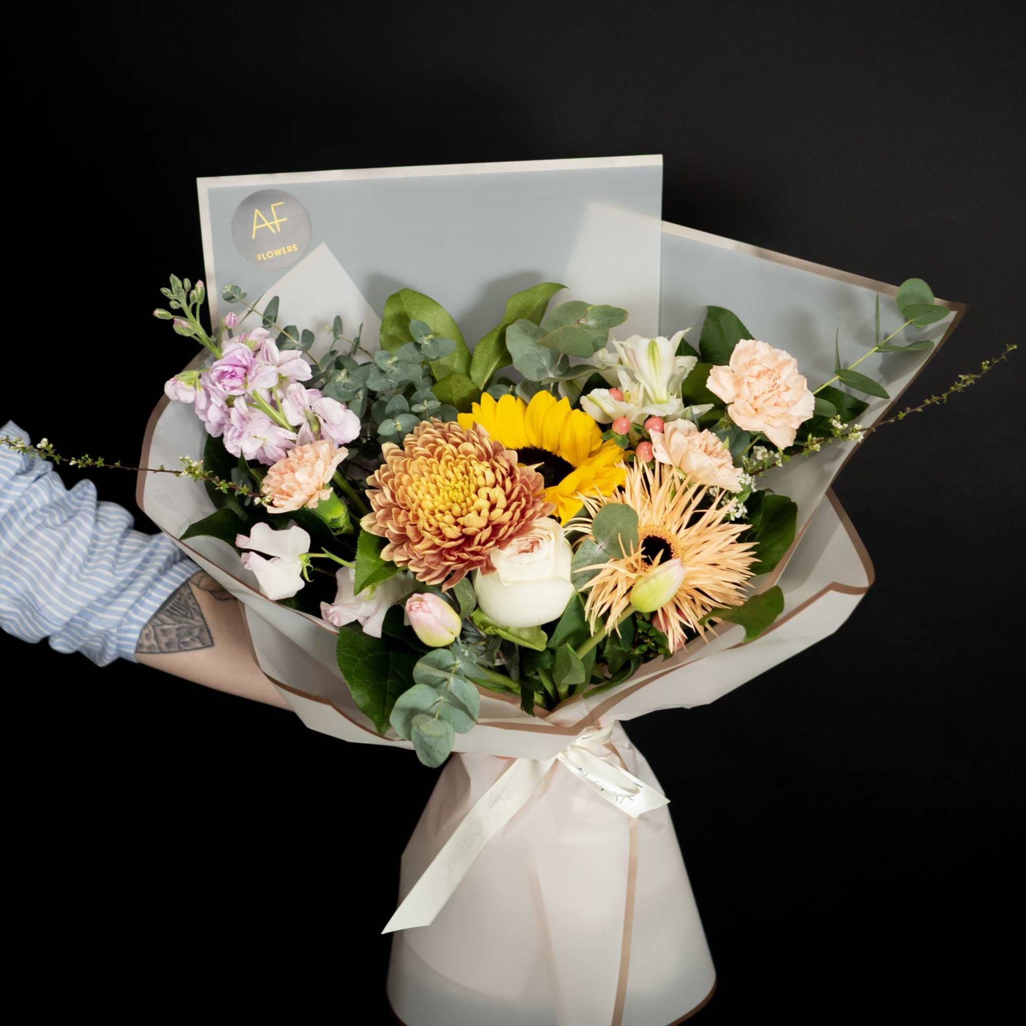 Mixed bouquet with sunflowers, chrysanthemums, and pale pink blooms in paper wrap