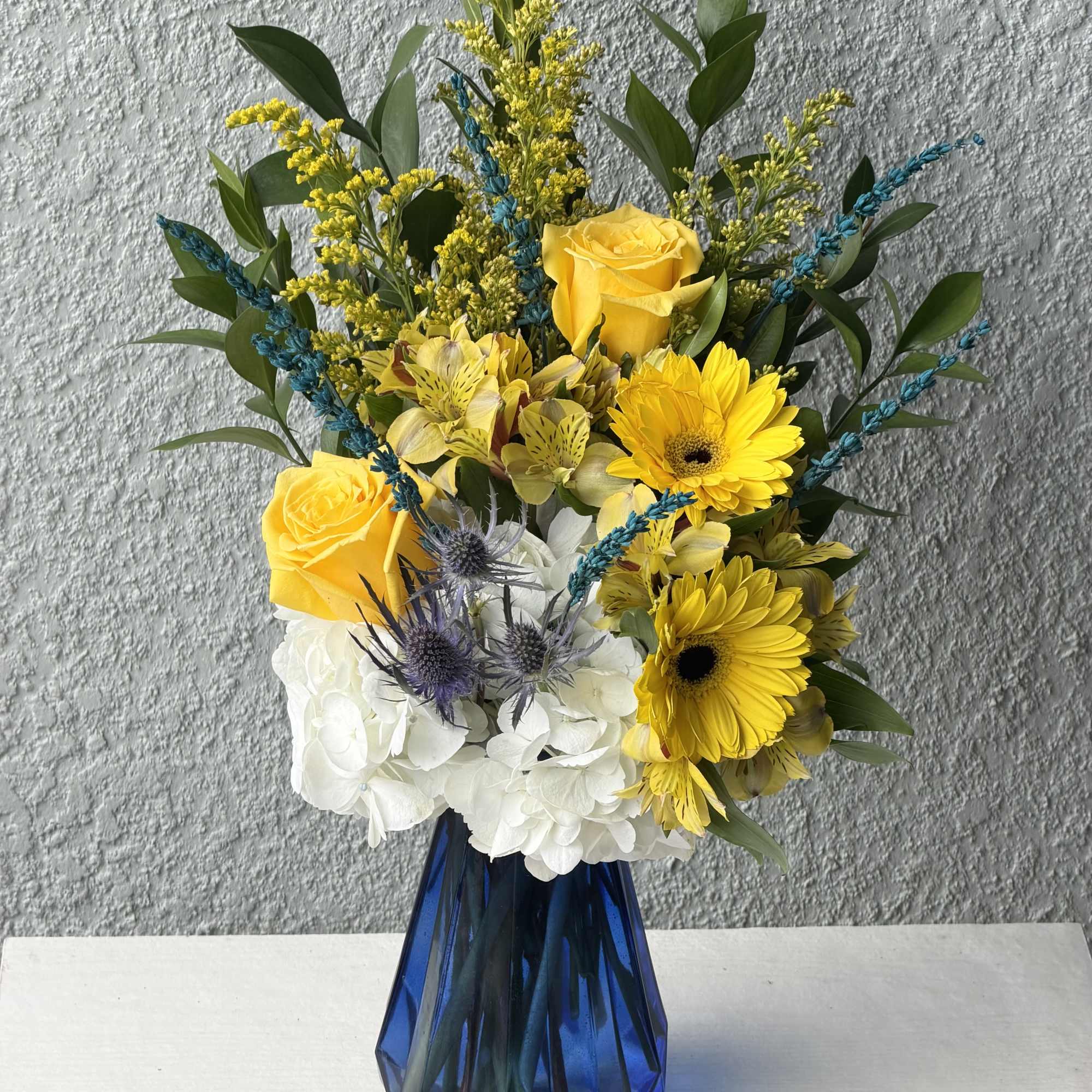 Bright yellow roses and gerbera daisies pop against billowy white hydrangeas and