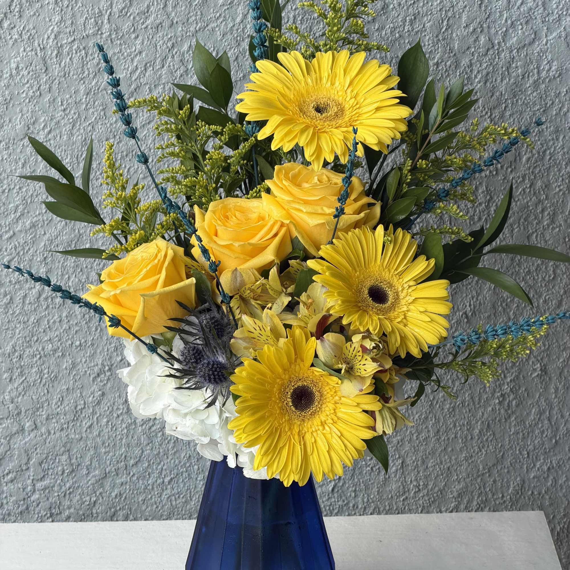 Yellow gerbera daisies and roses in a blue vase