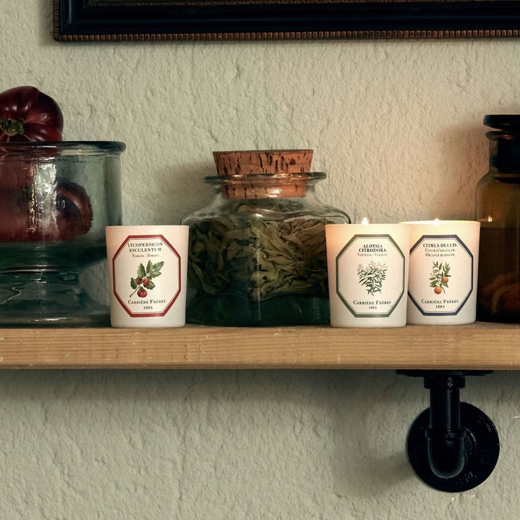 Three scented candles on a shelf beside glass jars