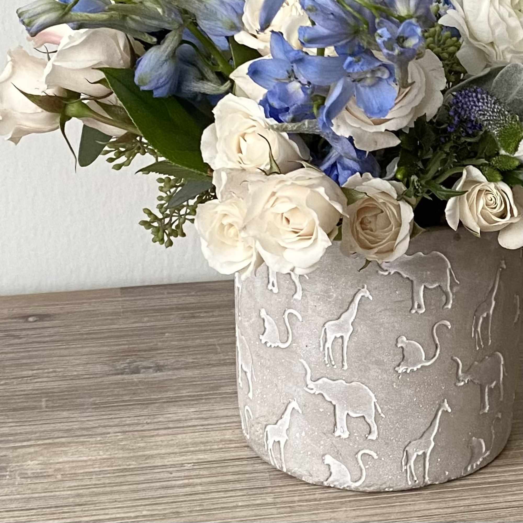 White roses and blue flowers in a gray animal-patterned vase