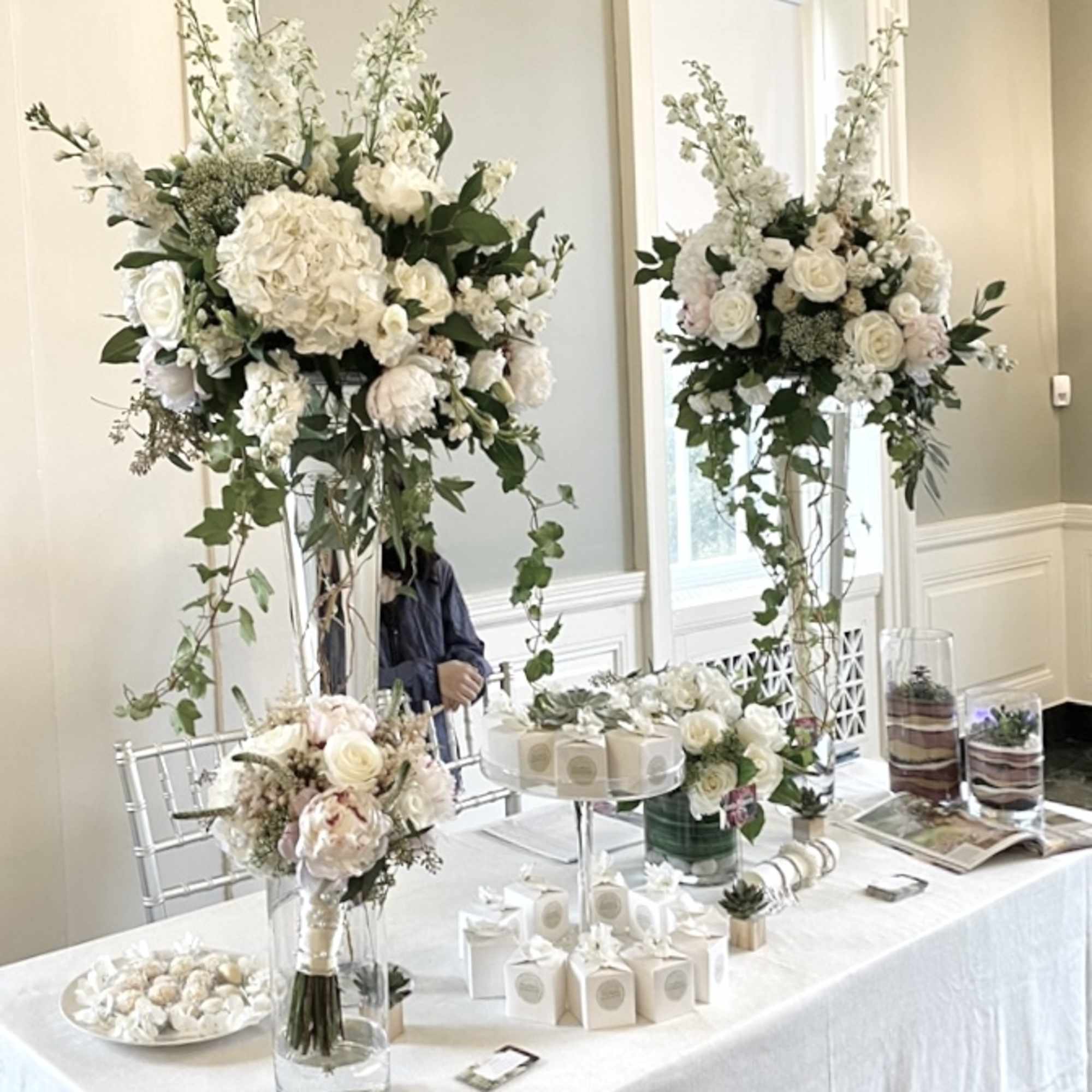 Tall white floral centerpieces on a decorated table with small gift boxes