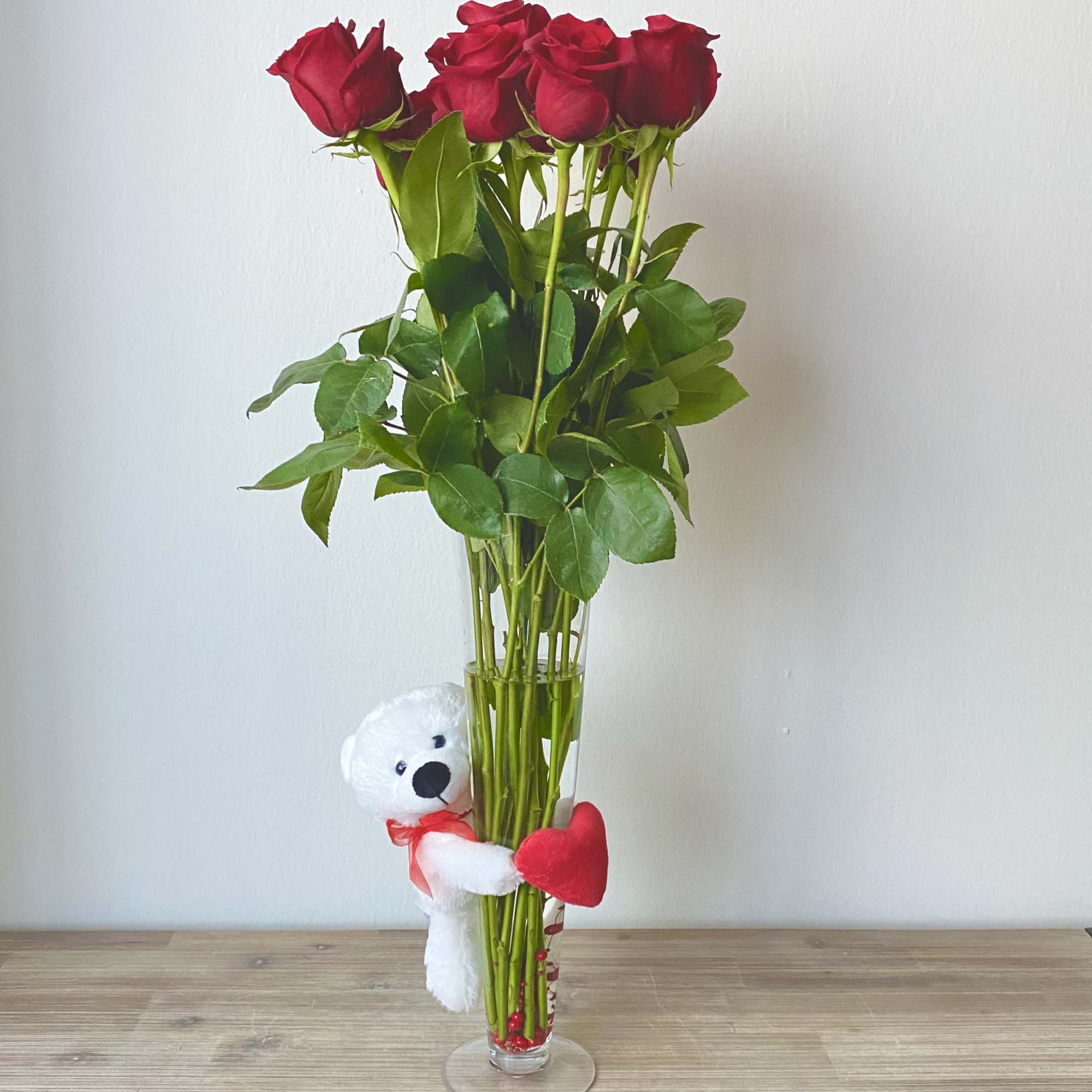 Tall vase of red roses with a small teddy bear and heart accent