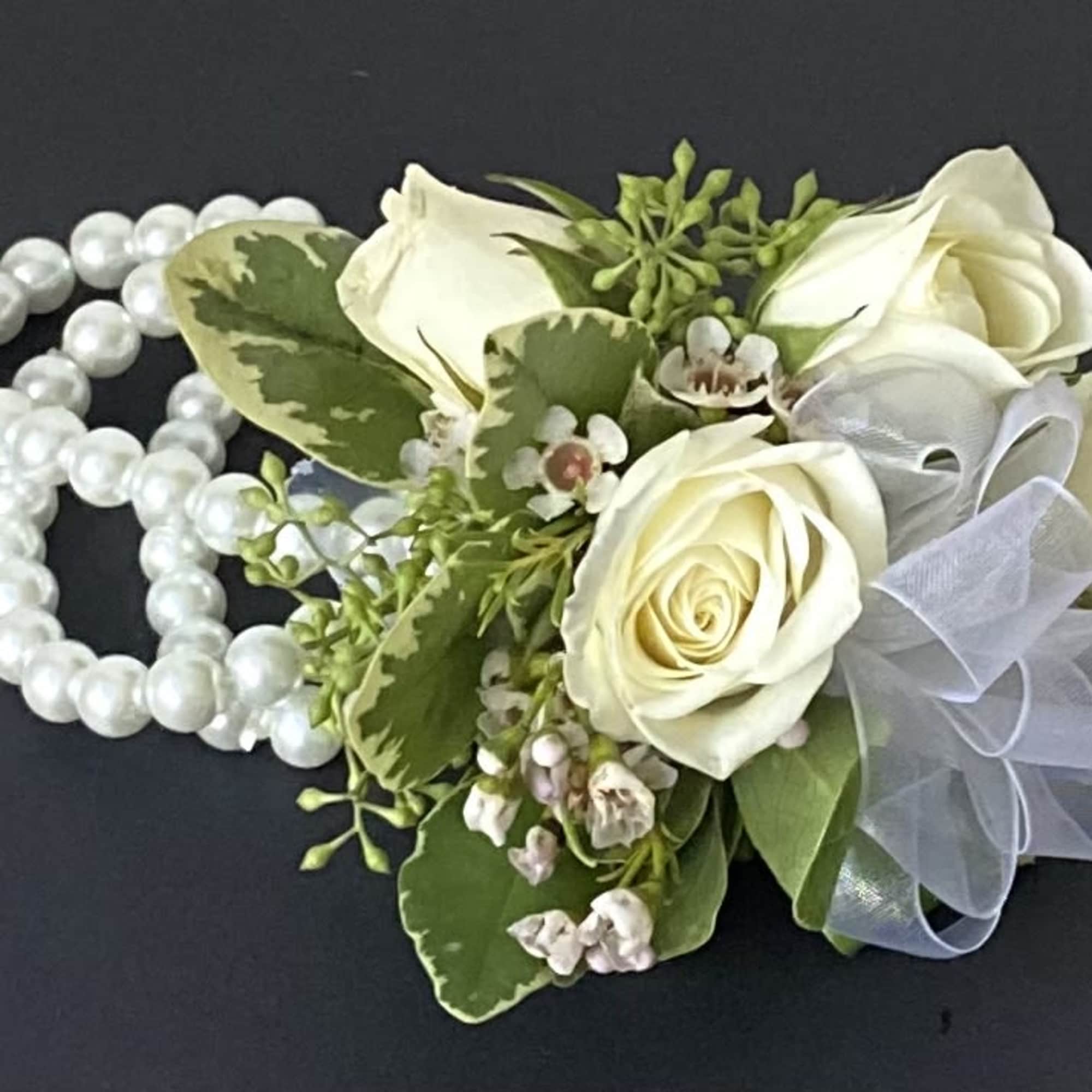 White rose corsage with pearl strands and a sheer ribbon on a dark background