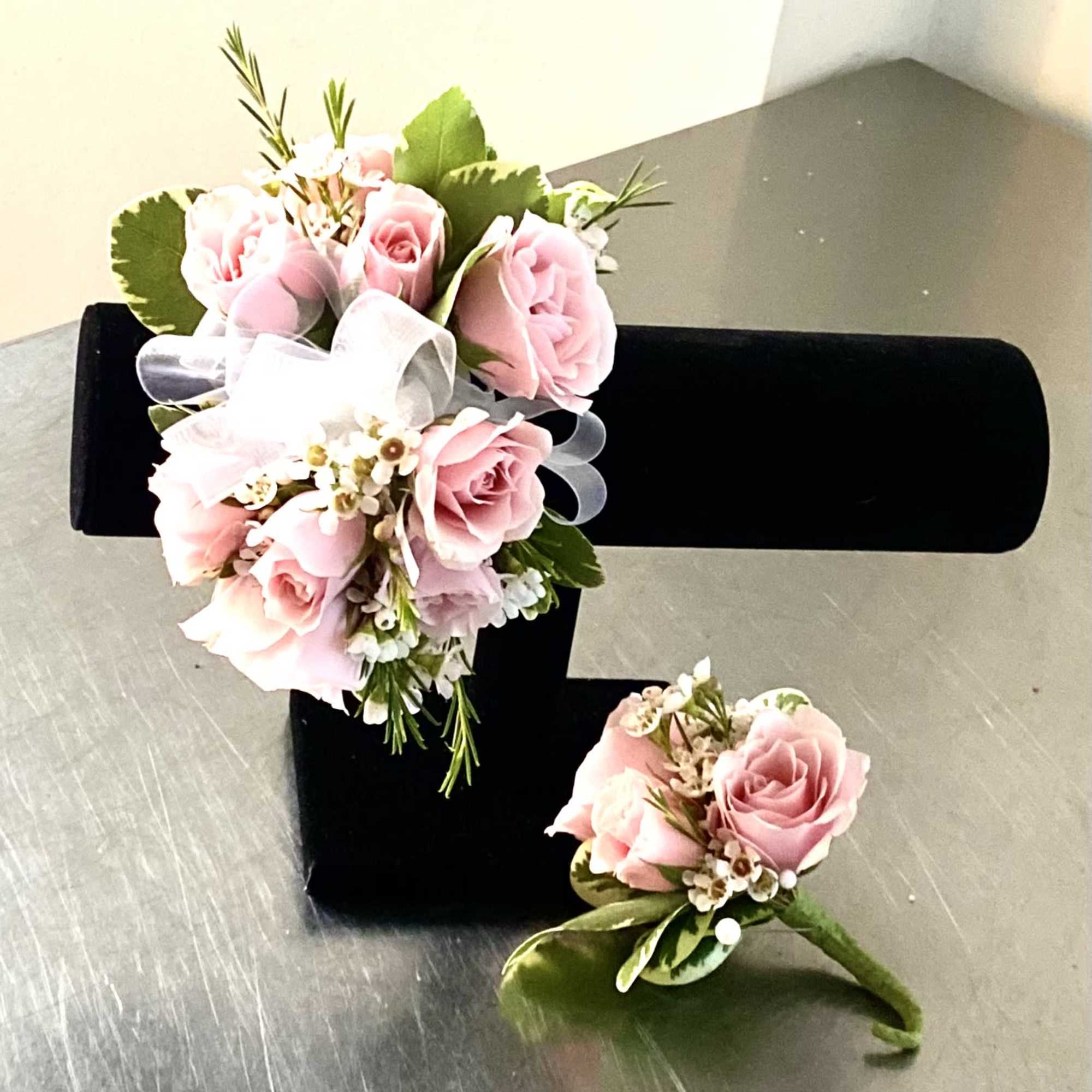 Pink rose corsage and boutonniere with white ribbon on a black display stand