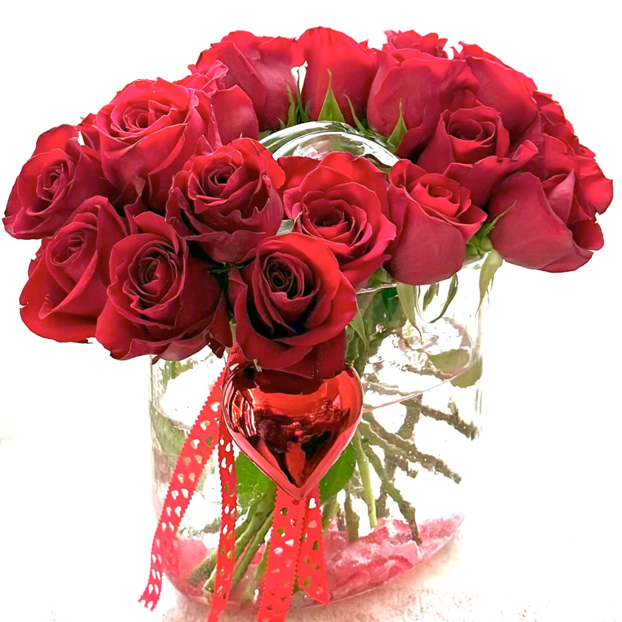 Red roses arranged in a clear glass vase with a red ribbon and heart ornament