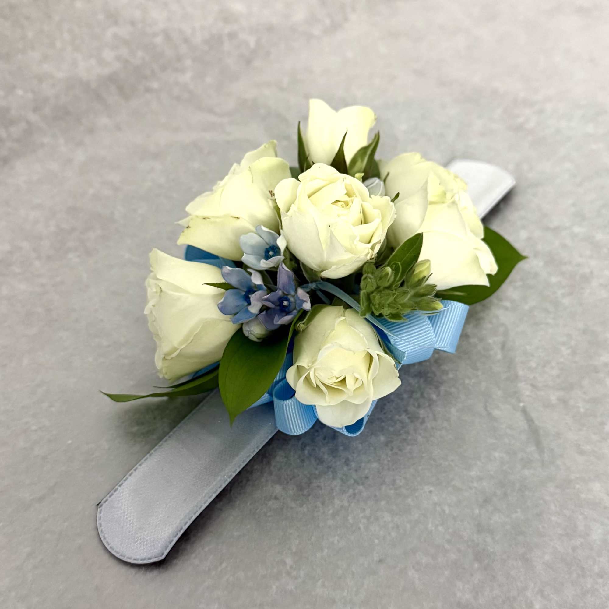White rose wrist corsage with blue ribbon on a satin band