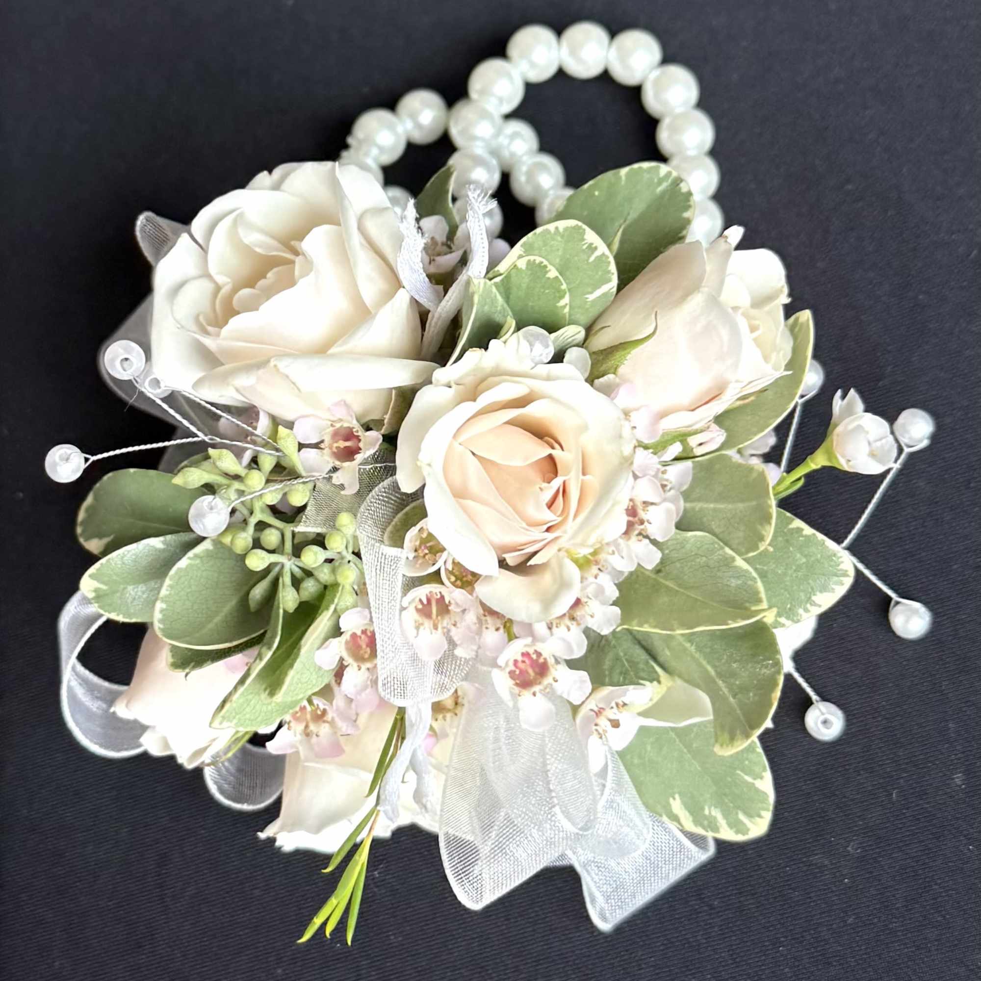 Cream rose corsage with pearl accents and ribbon on a dark background